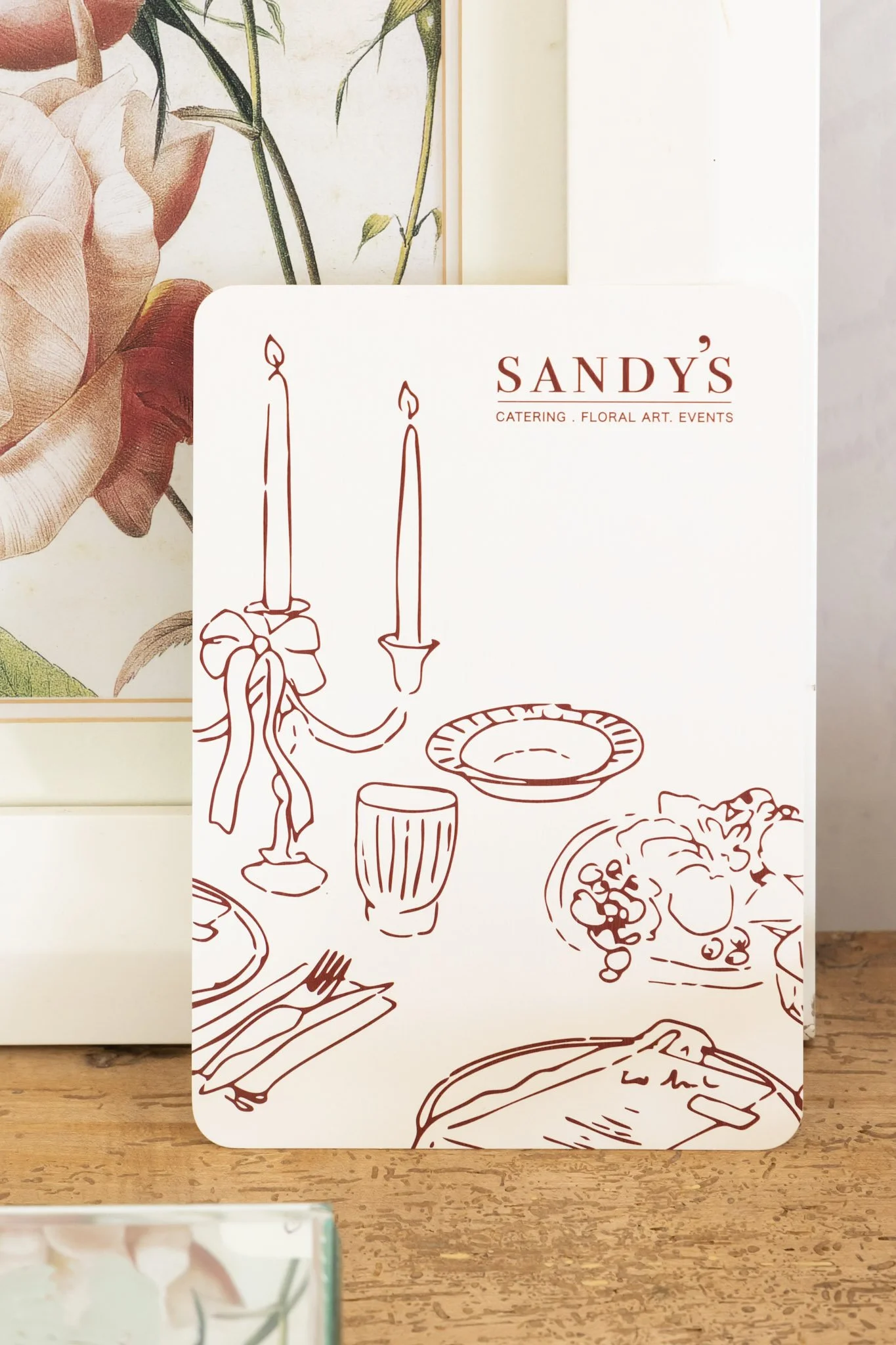 Close-up of a menu or brochure from Sandy's catering and floral arts event service with illustrations of candles, tableware, and food items.