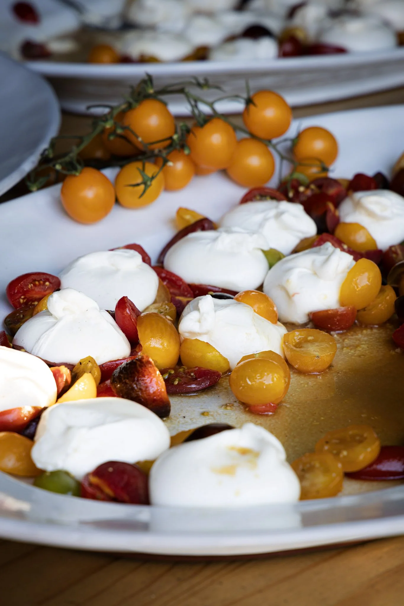 A plate of cherry tomatoes, sliced red and yellow peppers, fresh mozzarella cheese, and basil leaves on a wooden surface.