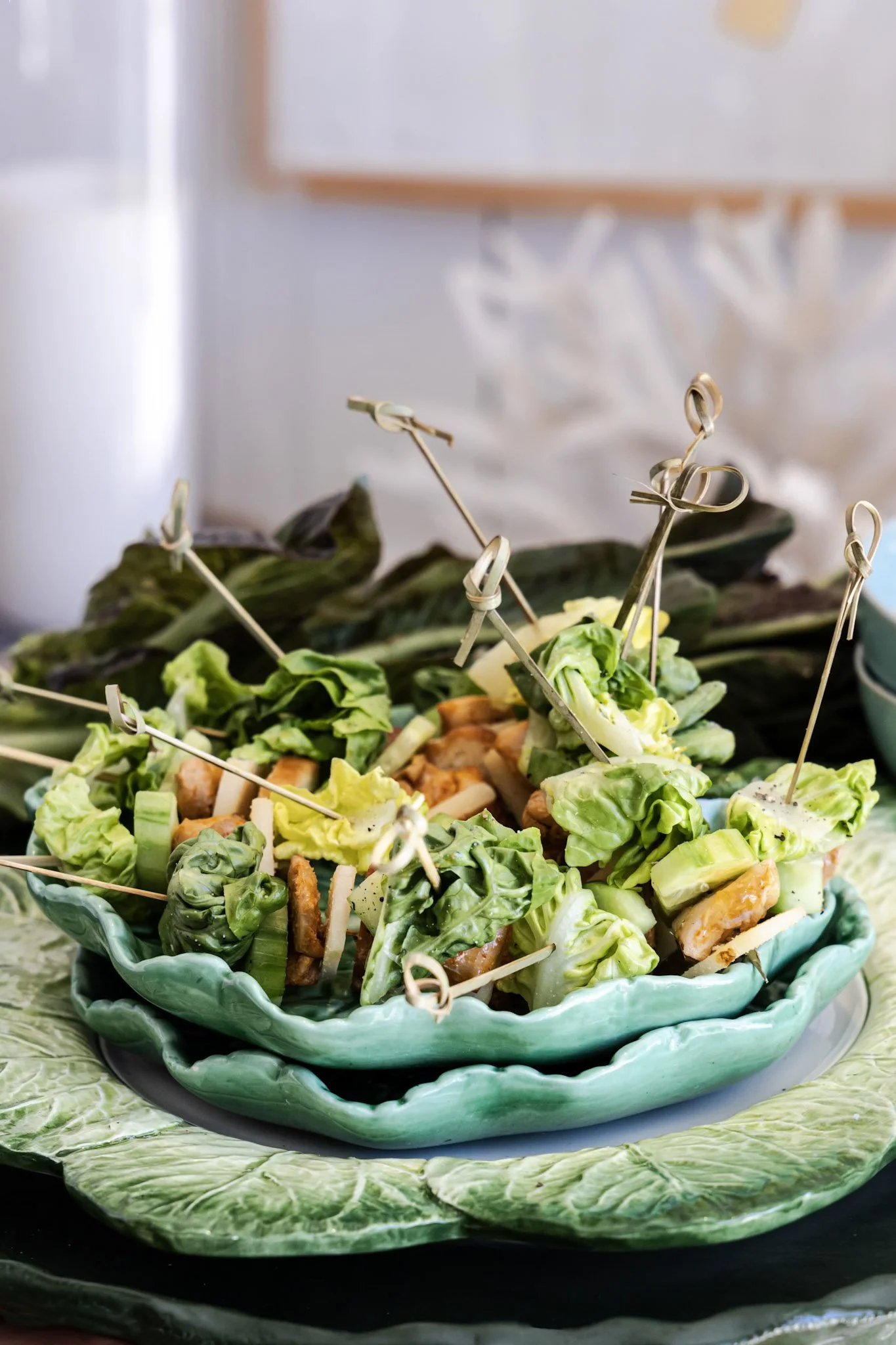 A layered serving platter with fresh vegetables, cut into bite-sized pieces, arranged on decorative green plates. The top layer has skewers with vegetables inside.