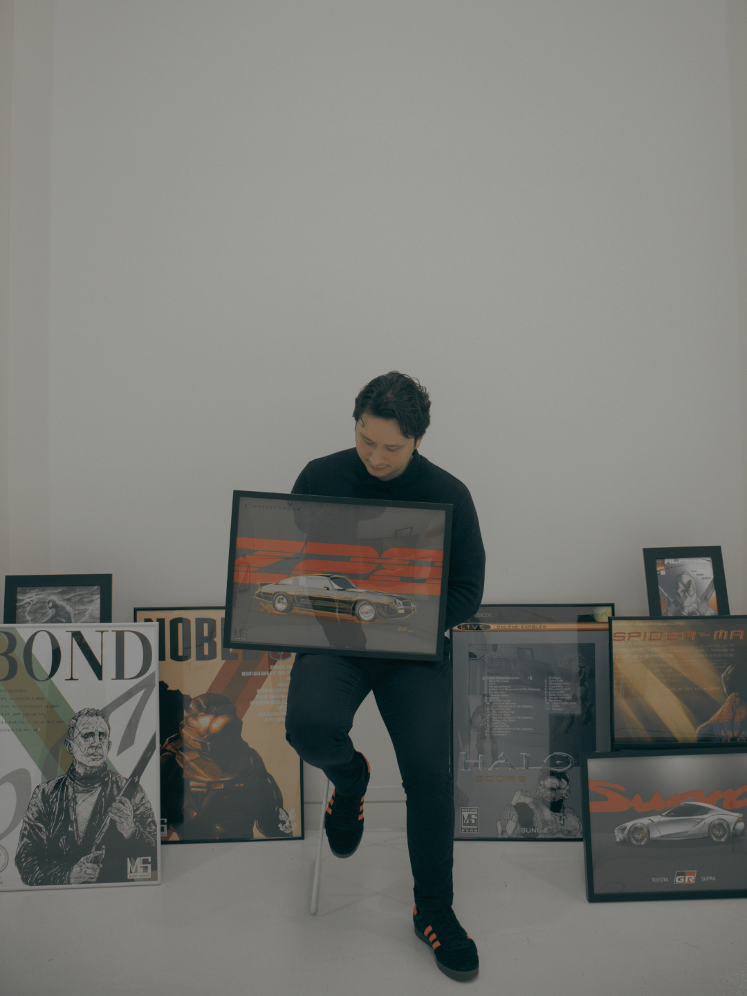 Person holding framed artwork of a race car, surrounded by various posters of video game characters and cars in a white room.