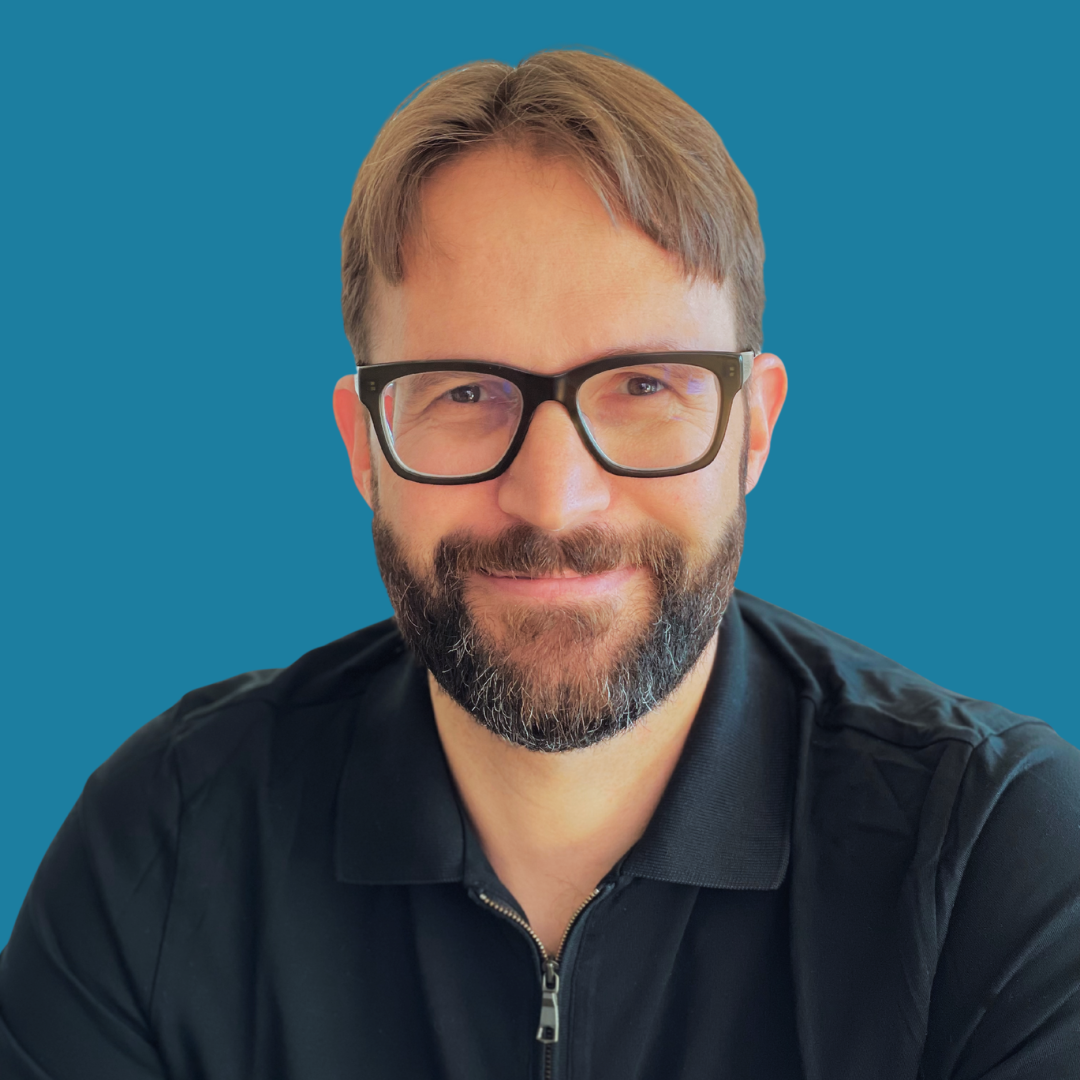 Jeff Ross, co-founder and managing partner of Nexuspoint in Dubai. A man with glasses and a beard smiling against a blue background.
