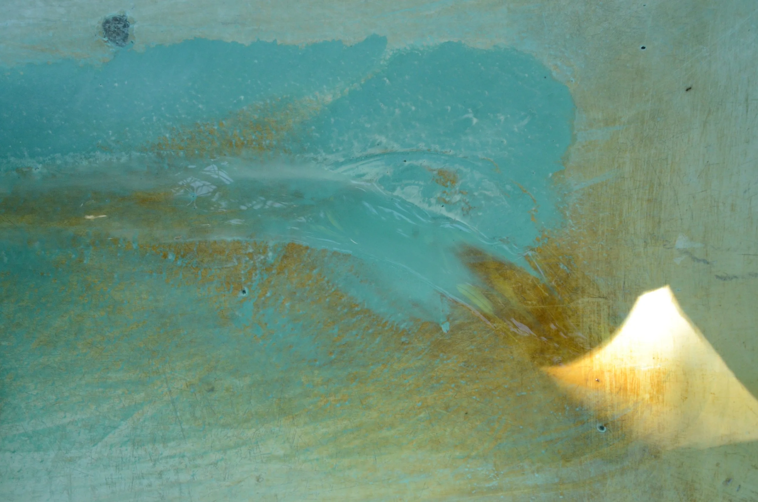 Close-up of a weathered, painted wall with a mix of teal and beige colors, showing areas of peeling paint and minor stains.