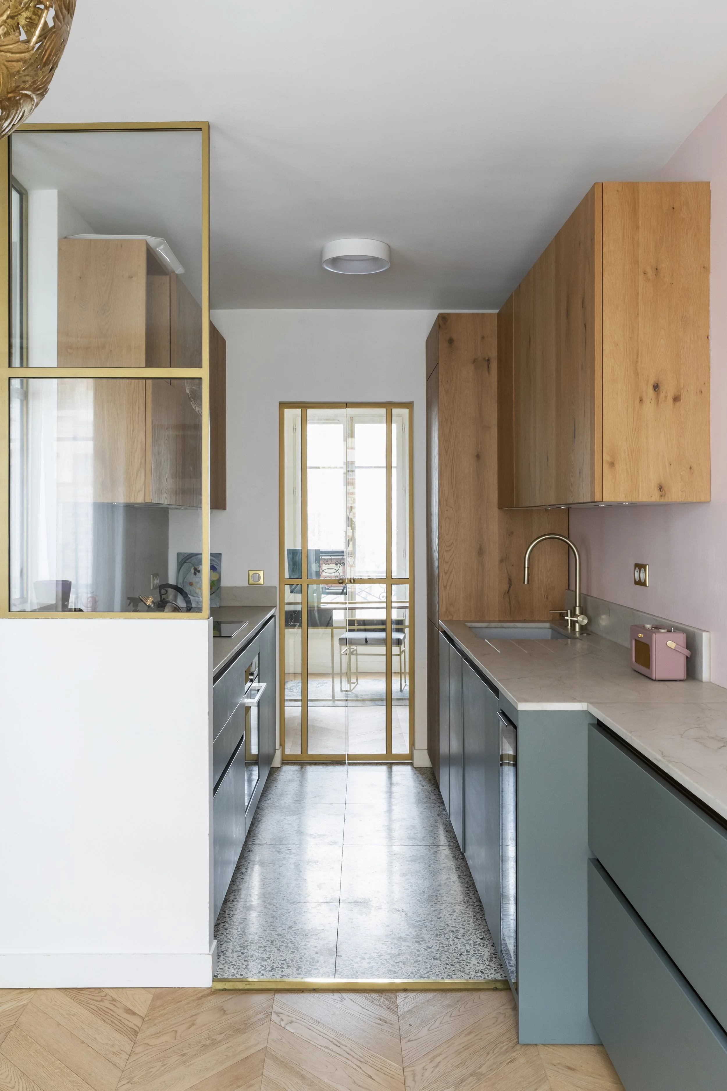 Cuisine moderne avec armoires en bois, éléments gris, comptoir en marbre, et fenêtre laissant entrer de la lumière naturelle.