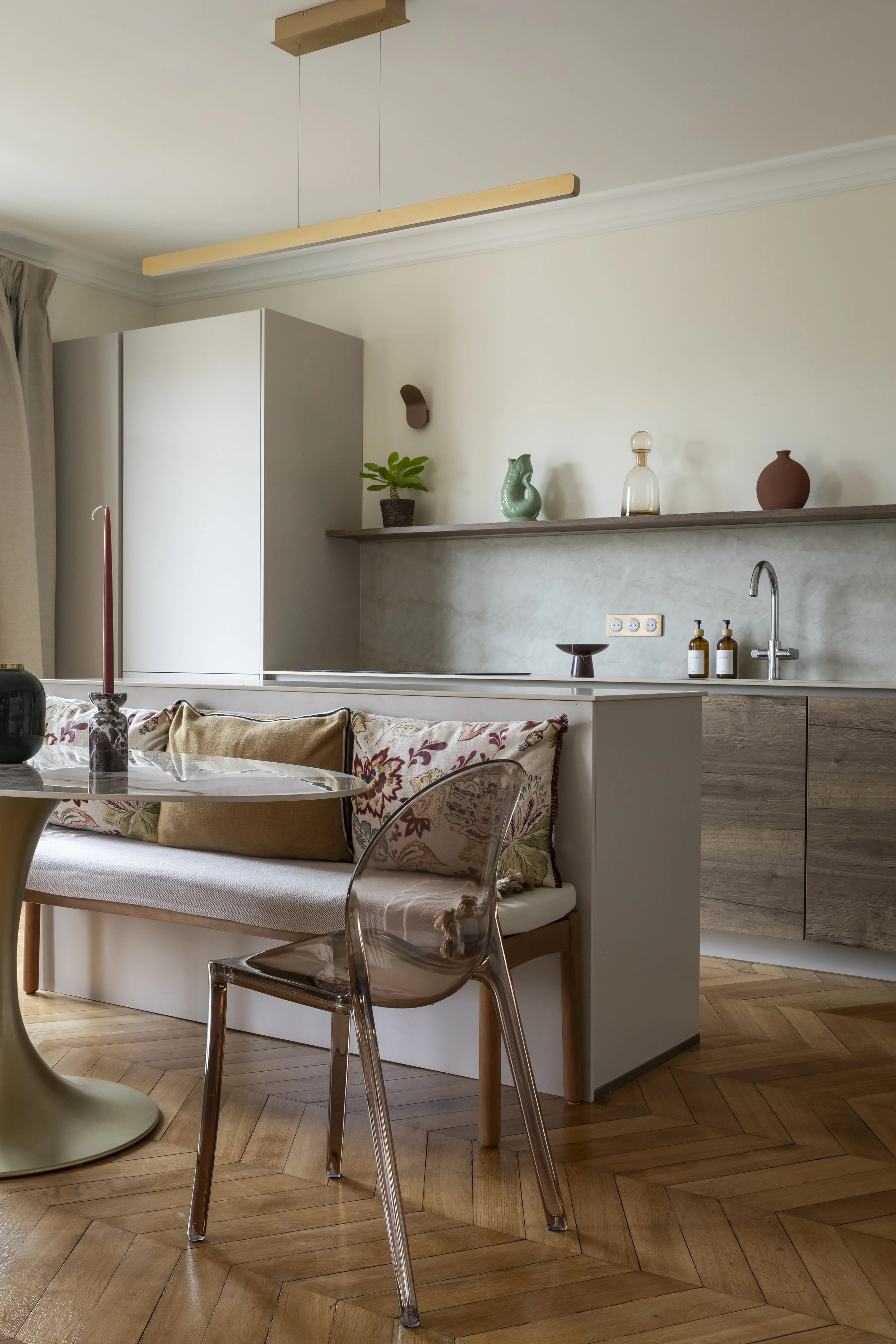 Une cuisine moderne contemporaine avec îlot central installée dans la pièce à vivre d'un appartement familial dans l'ancien, dans la avec une table à manger au pied circulaire doré et plateau ovale en céramique entourée de chaises en plastique polypr