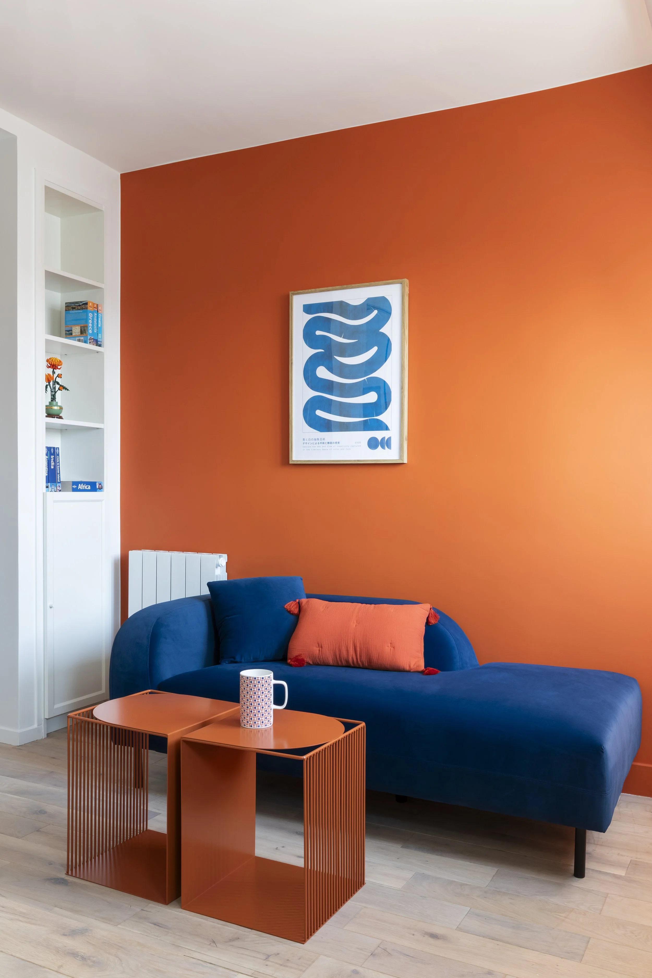 Salon avec un mur orange, un canapé bleu avec un coussin orange, une table basse orange et une affiche au mur représentant un serpent bleu.