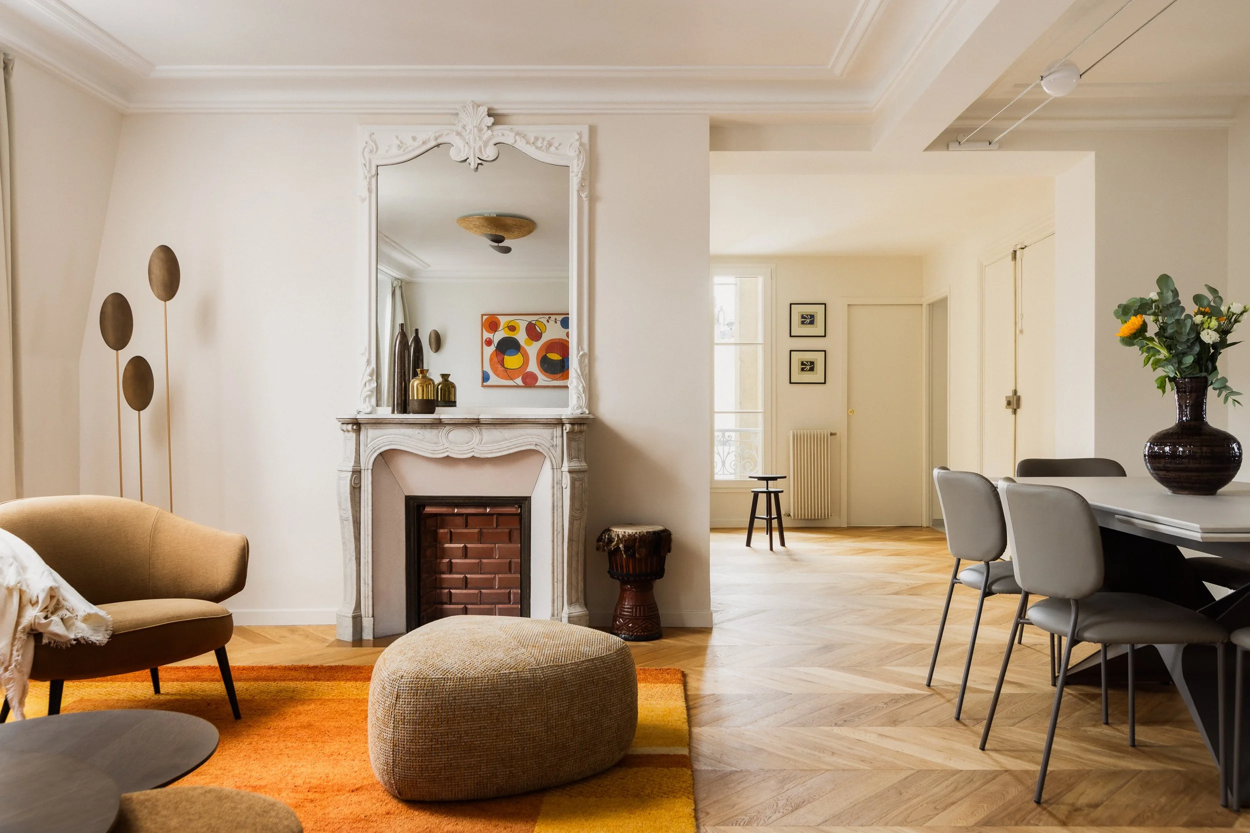 Pièce à vivre contemporaine dans appartement haussmannien avec table à manger extensible, pouf triangulaire aux angles arrondis de la marque Boconcept modèle Bermuda, lampadaire d'inspiration Art Déco, tables basses rondes gigognes en bois, objets dé