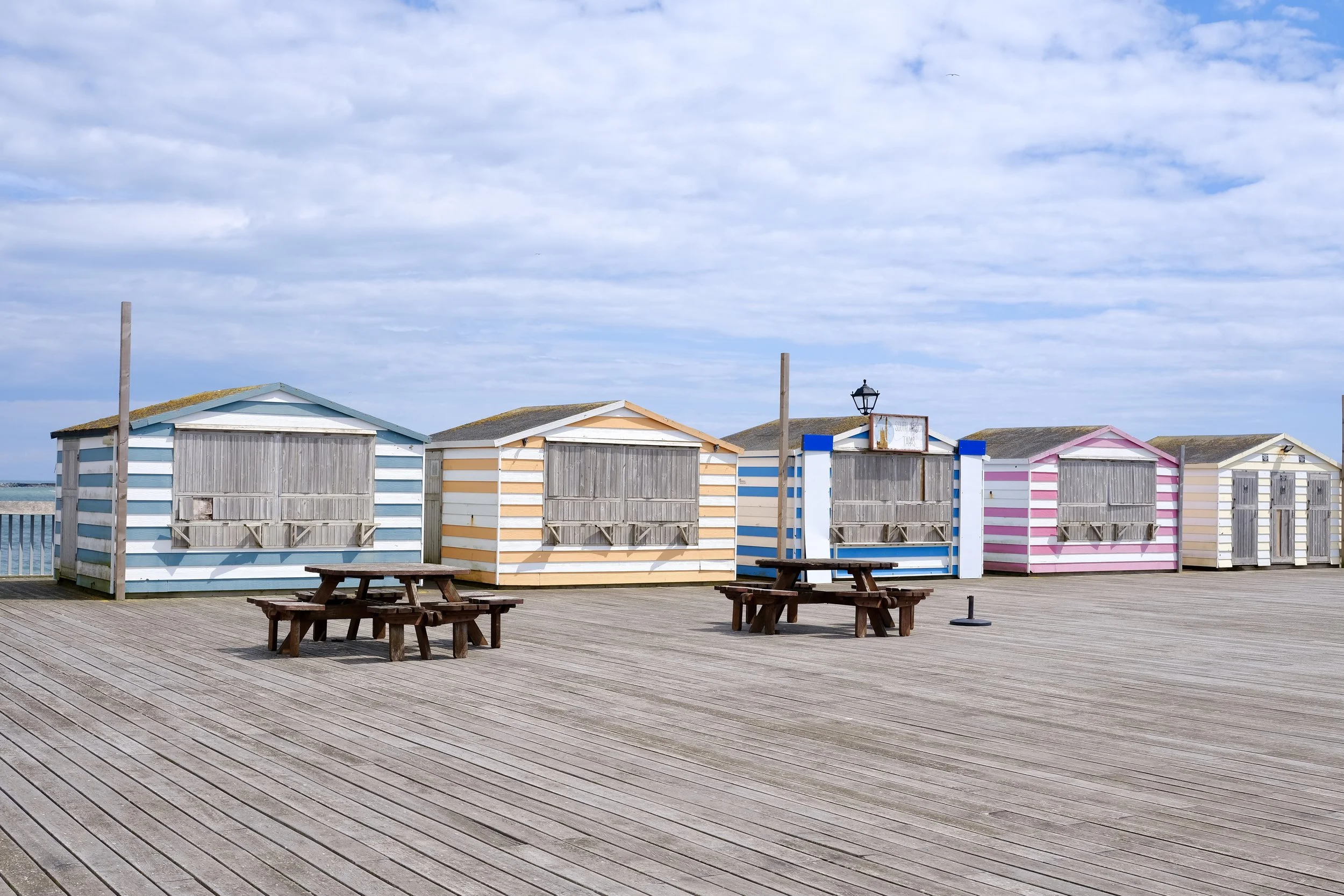 Colorful beach huts with striped patterns on a wooden pier under a cloudy sky.