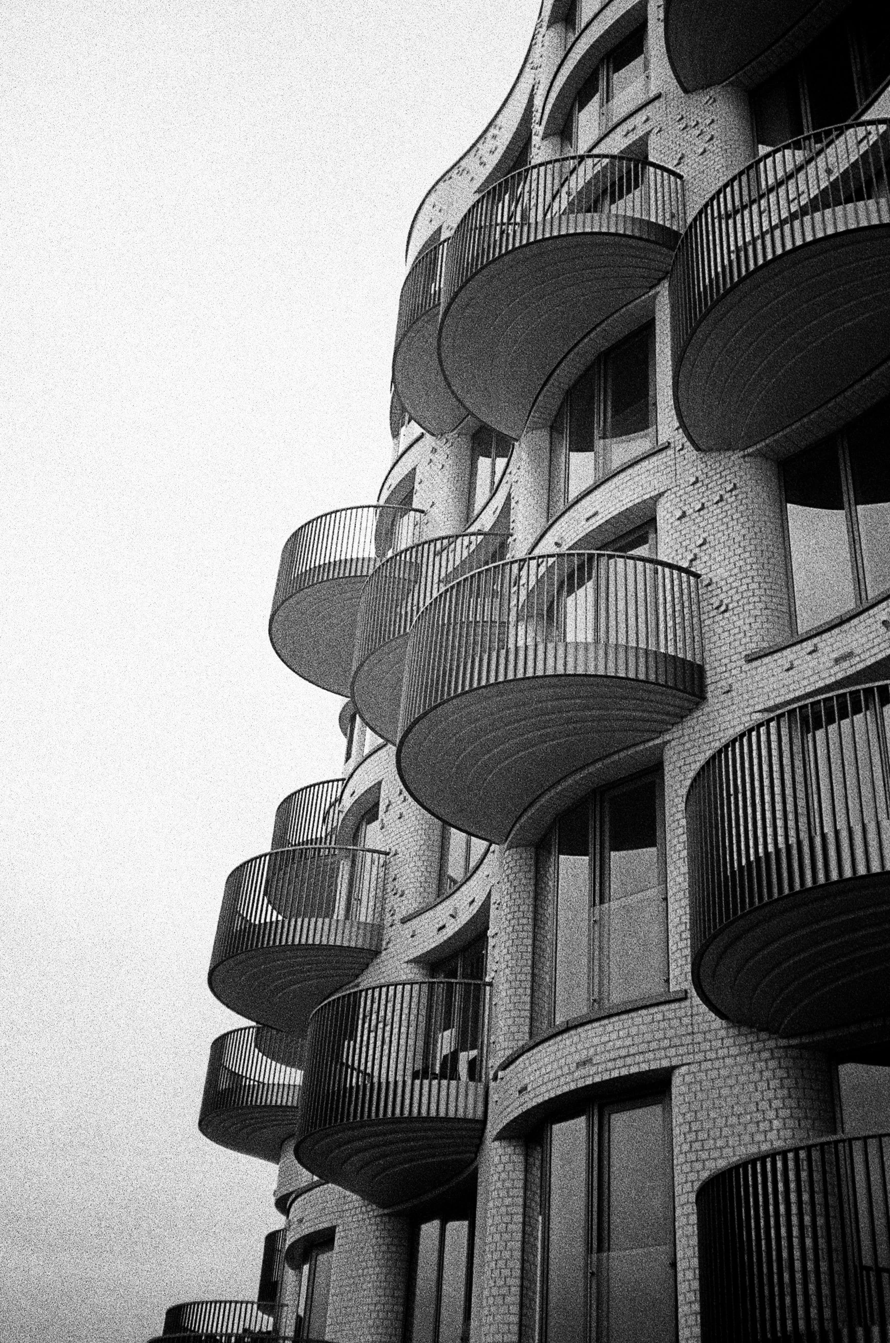Black and white photo of a modern multi-story apartment building with curved balconies and brick exterior.