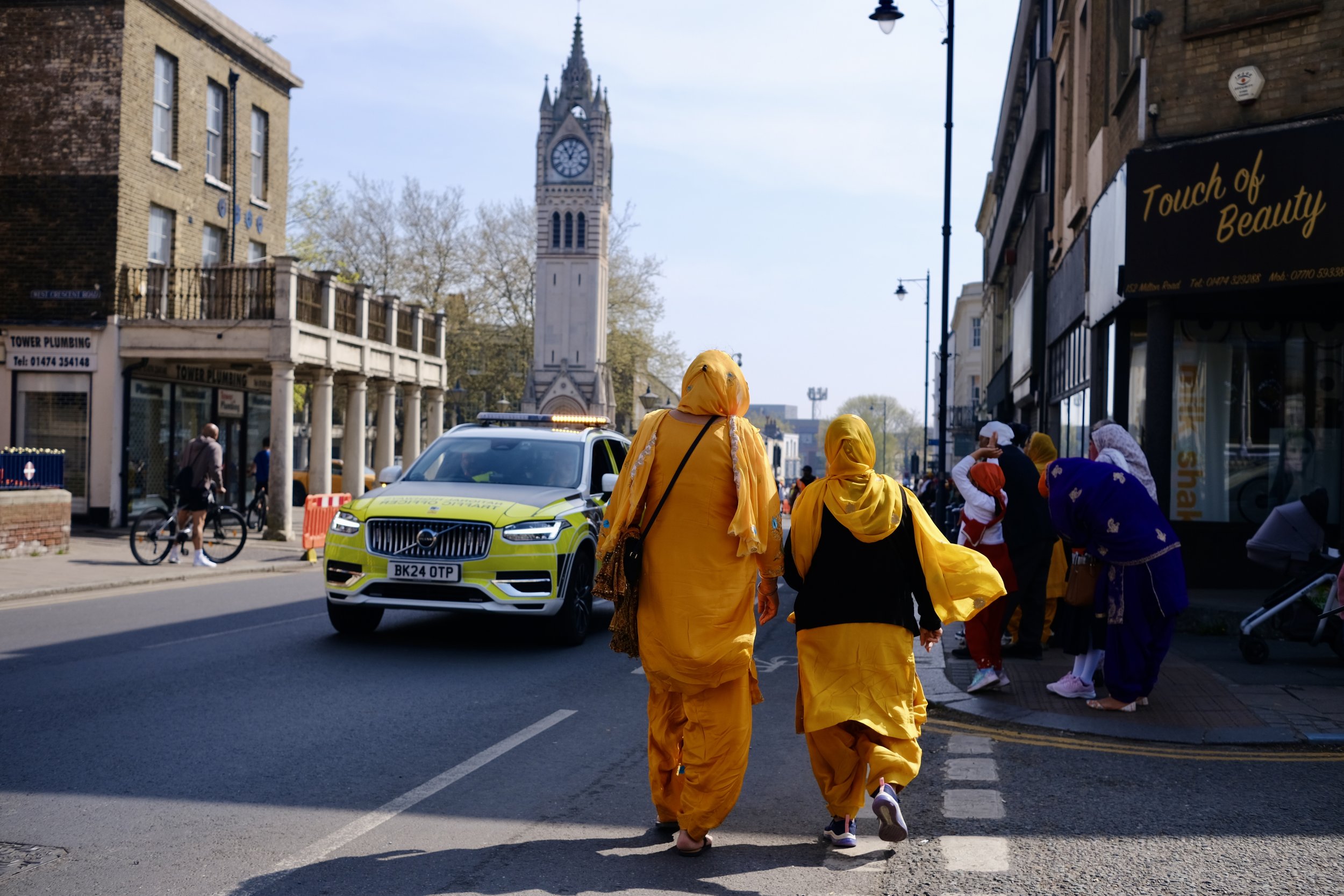 People dressed in yellow traditional attire walking on the street in front of a tall clock tower.