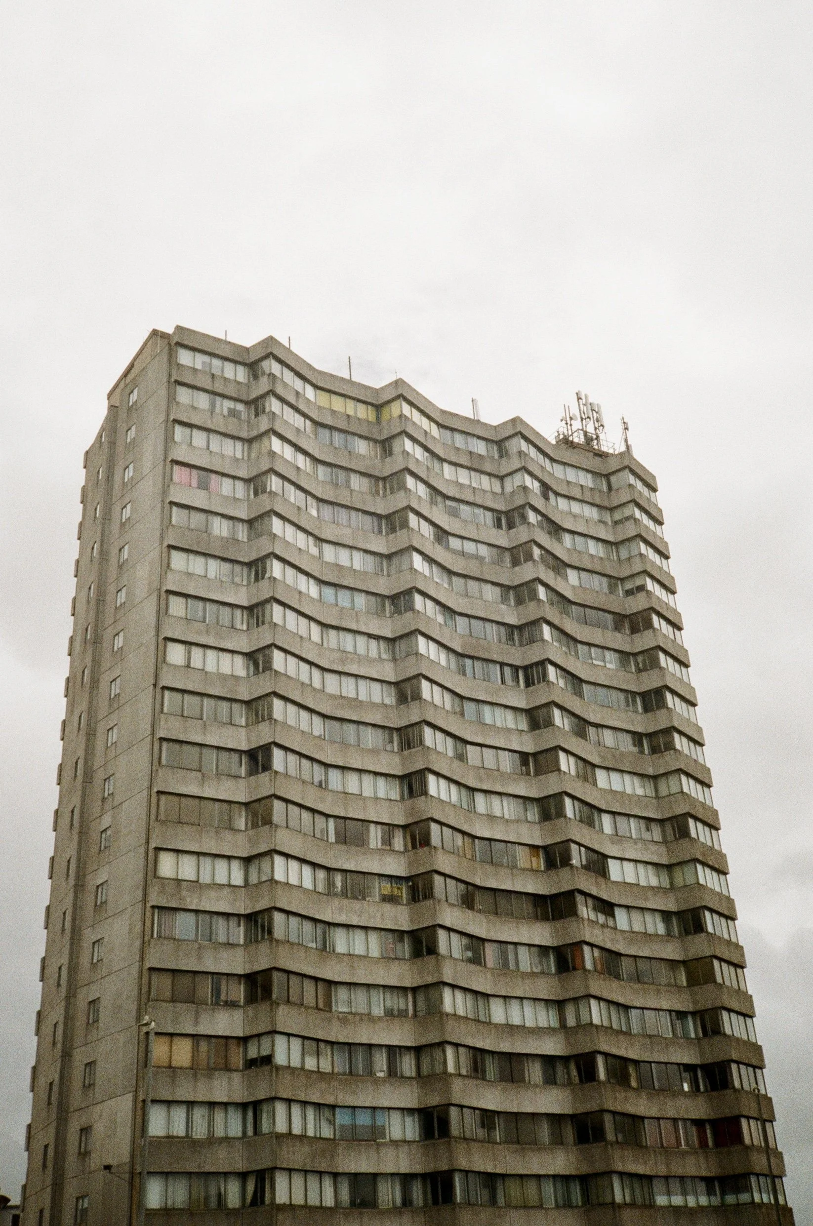 A tall, multi-story apartment building with a zigzagging design on the facade, featuring numerous windows and antennas on the roof.