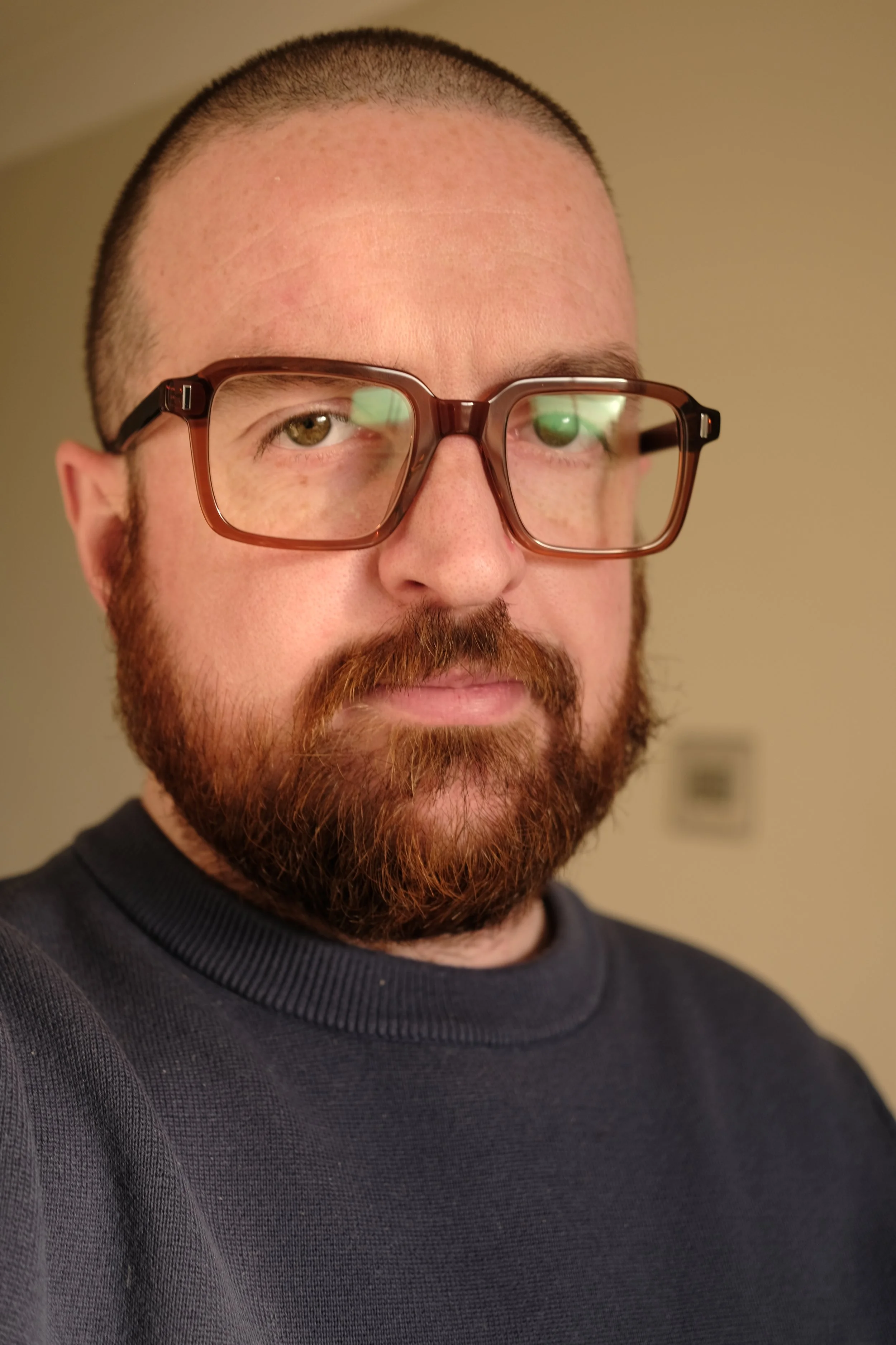 A man with a beard and glasses looking at the camera, wearing a dark sweater, with a neutral background.