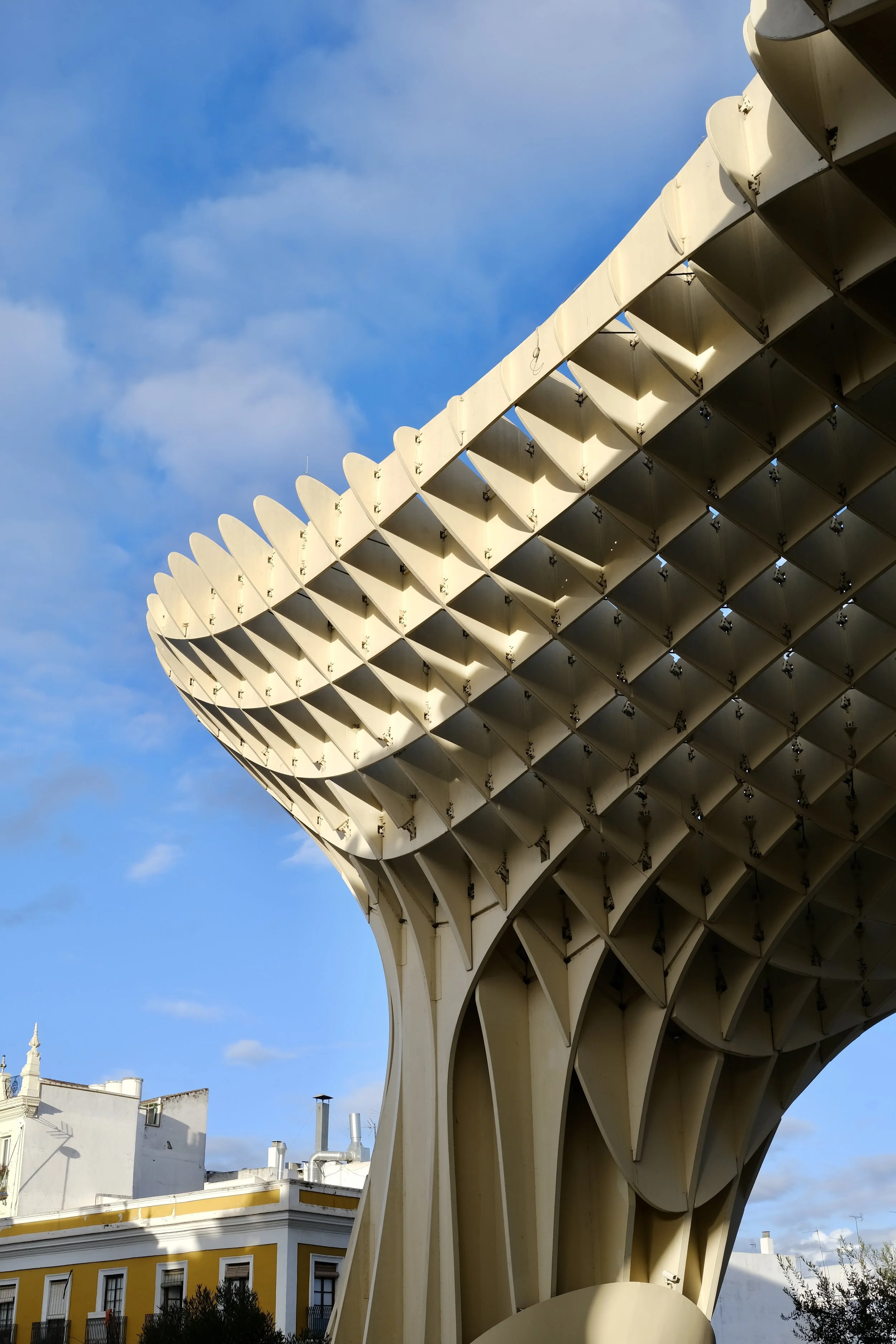 Architectural structure with curved, panel-like elements against a background of blue sky with clouds.