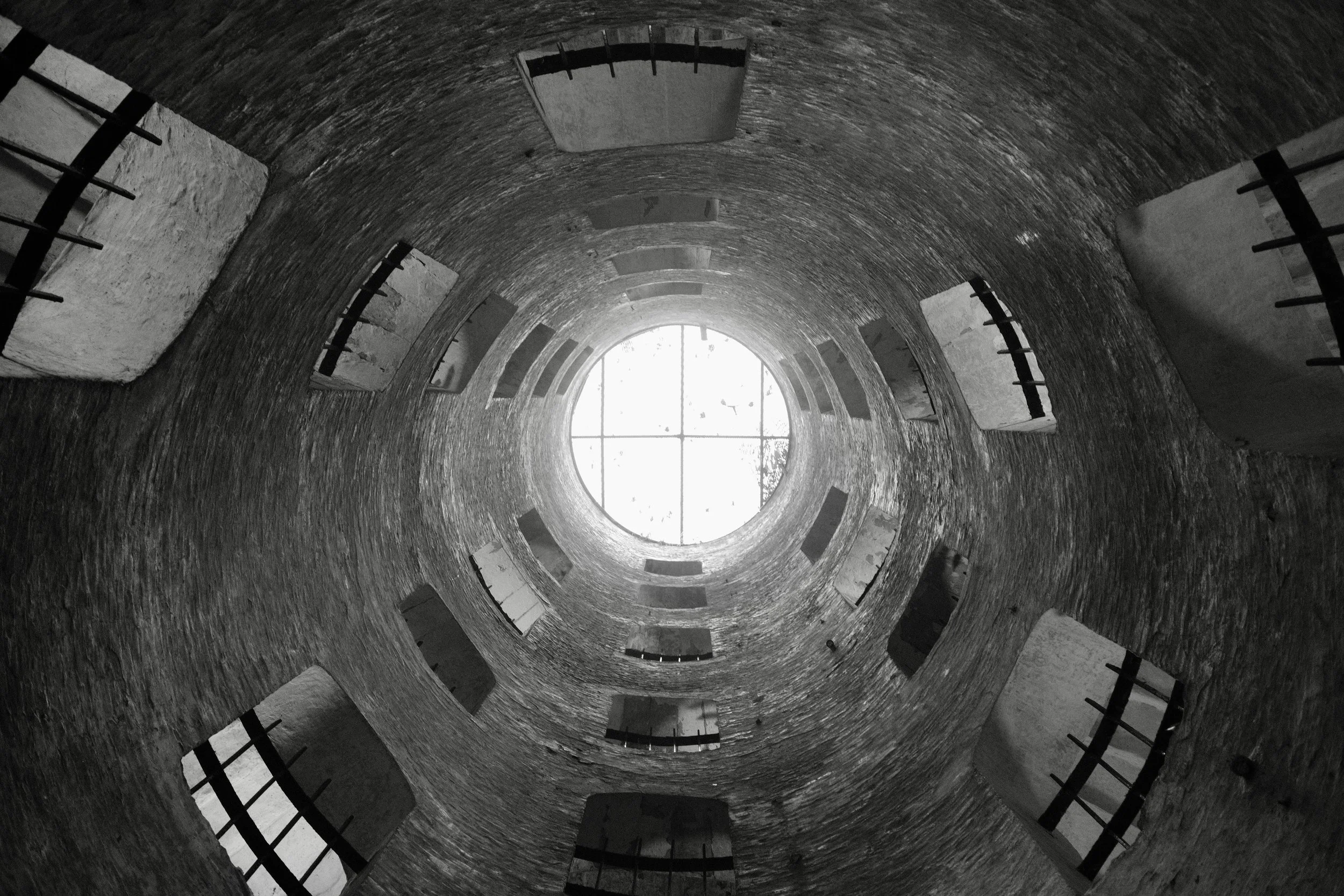 Looking up inside a circular brick tower through an opening at the top, with window panes visible and some furniture or construction materials around the edges.