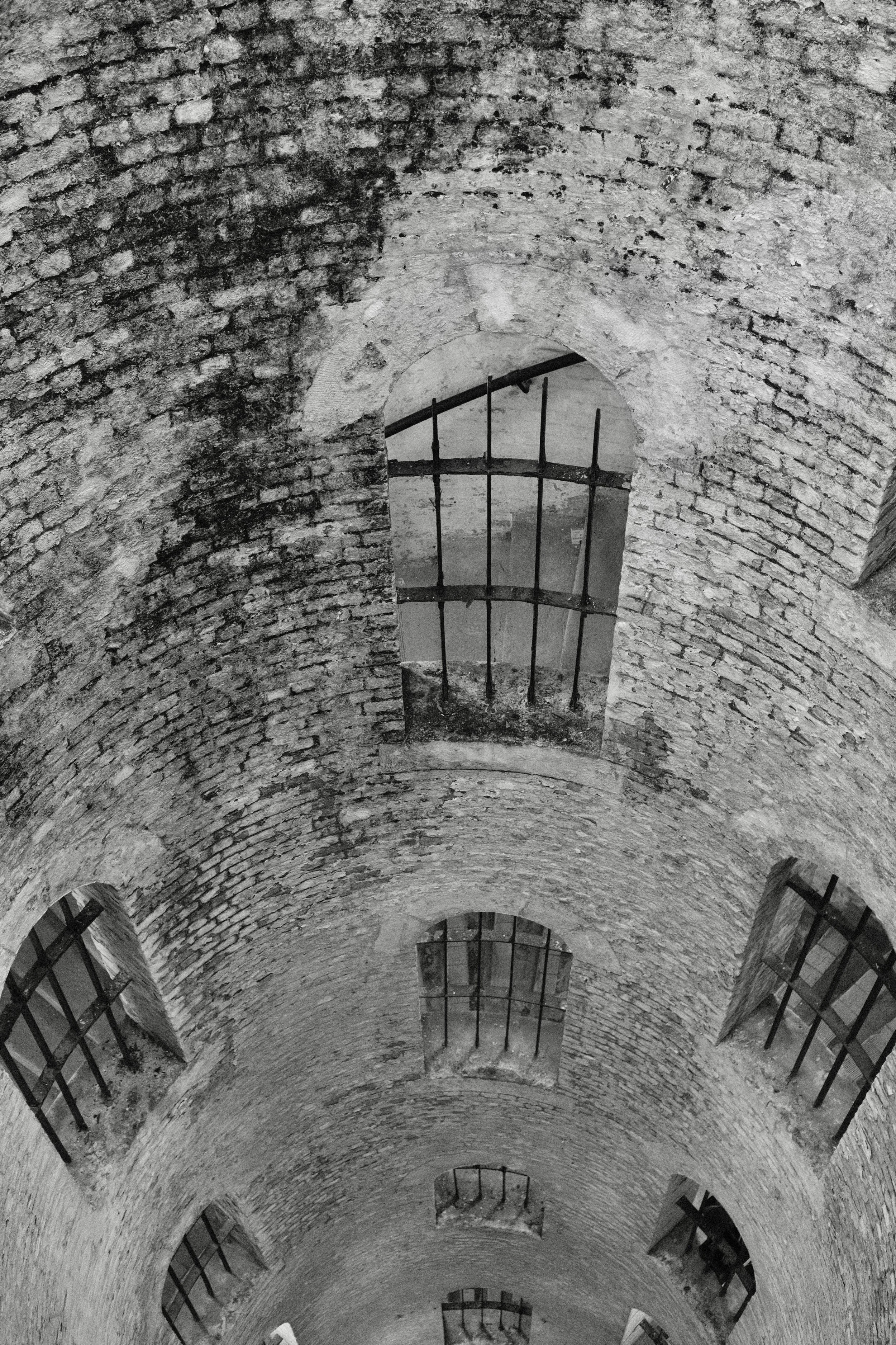 Interior view of a brick tunnel with small arched windows fitted with barred grates, showing a curved vaulted ceiling.
