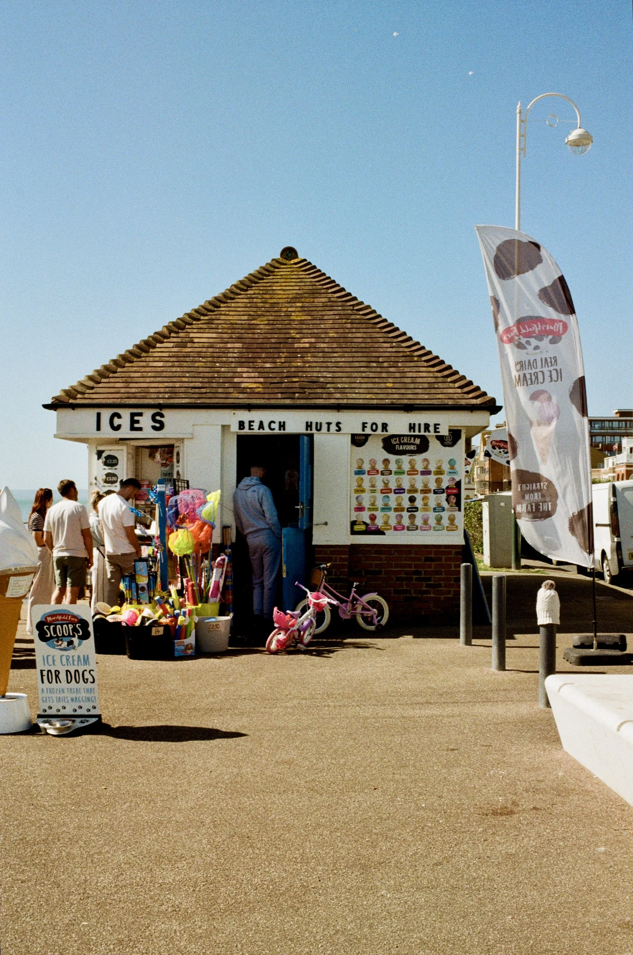 Beachside ice cream stand with colorful ice cream menu, children’s bikes, and a sign advertising ice cream for dogs.
