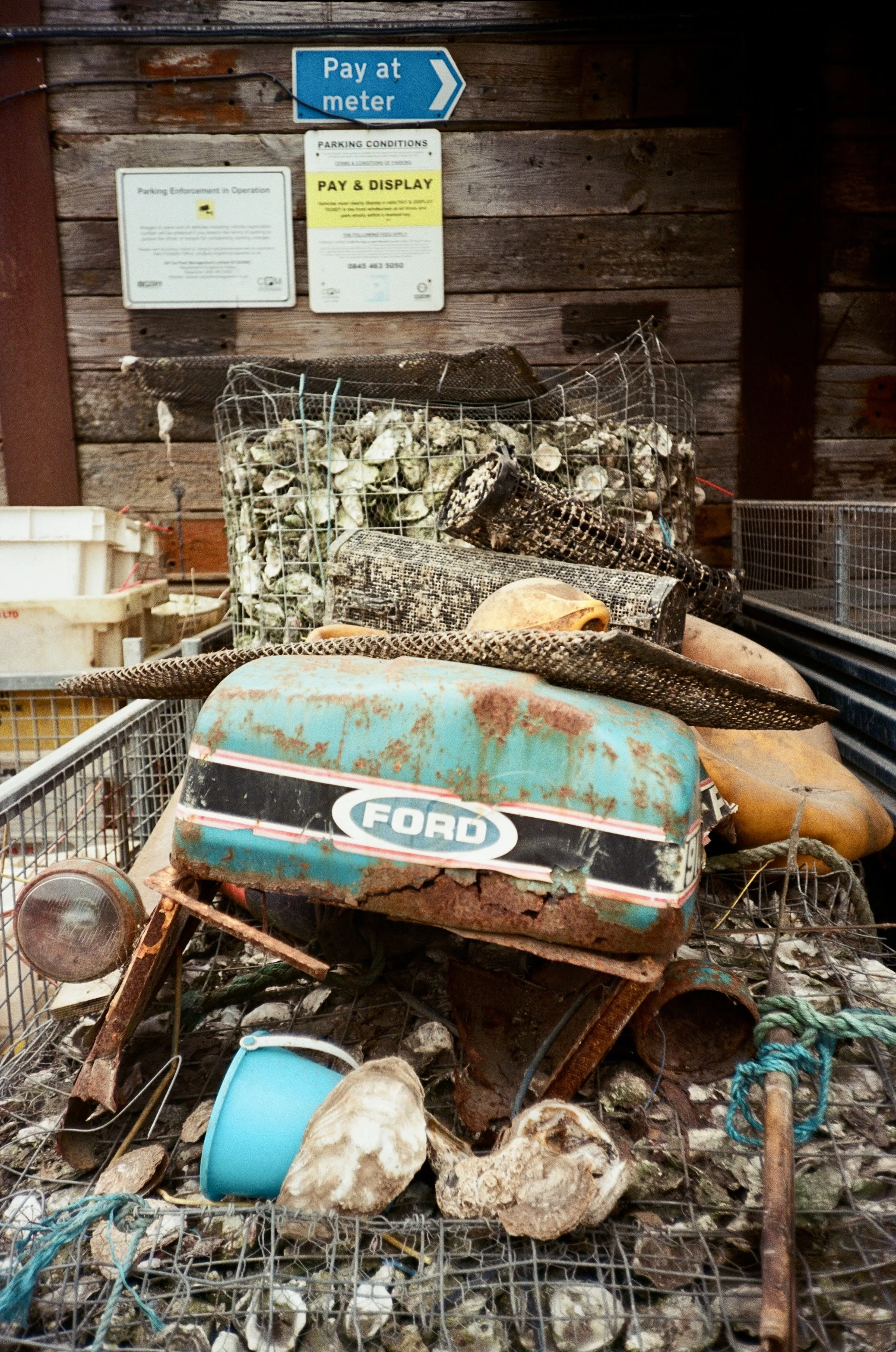 Old rusty toy car on a display shelf, surrounded by various debris including rocks, plastic containers, and scraps of wire.