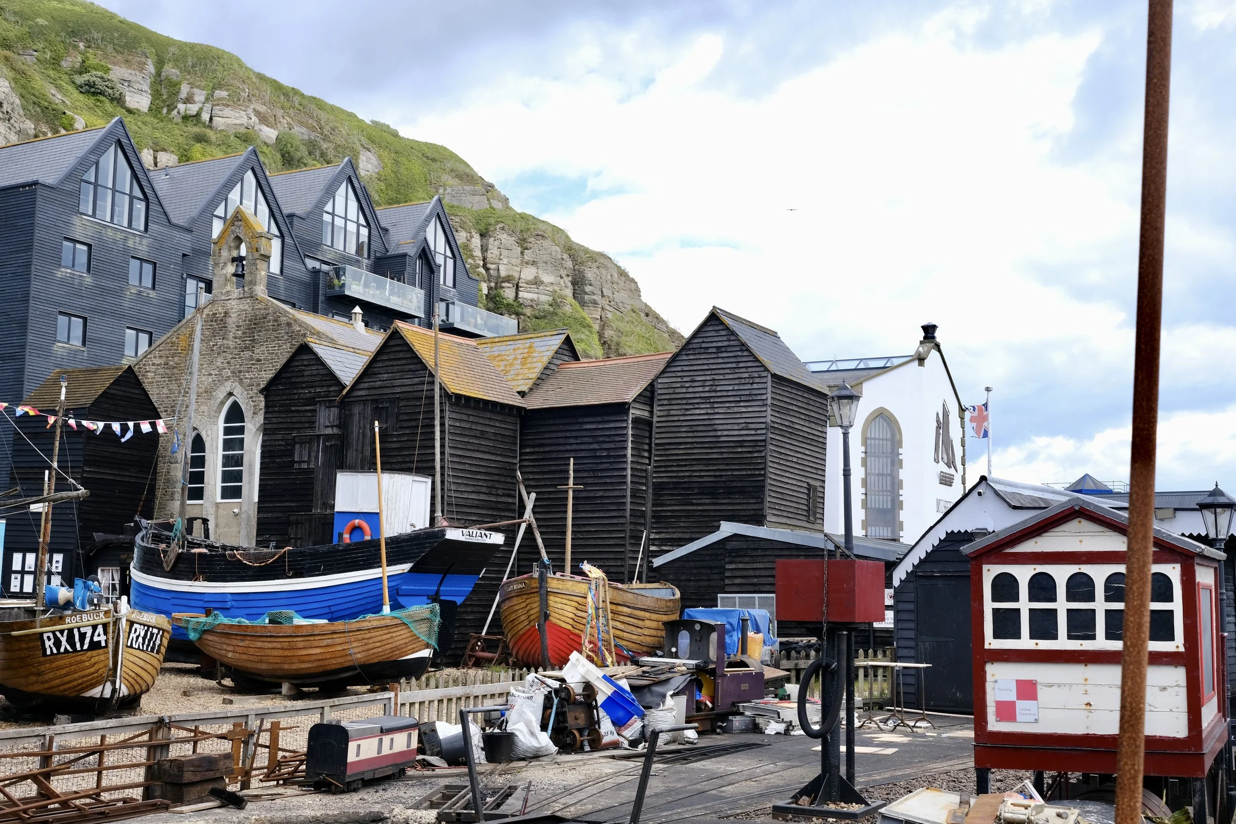 A harbor scene with boats and fishing equipment, surrounded by colorful buildings and a hillside with greenery.