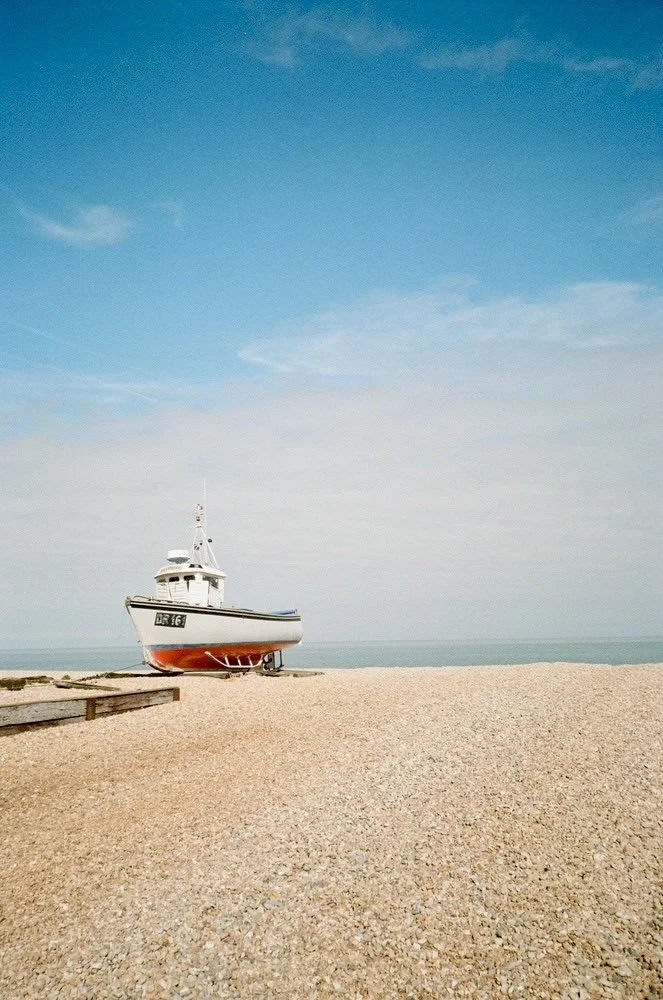 A small white boat resting on a pebbled beach with a clear blue sky overhead.