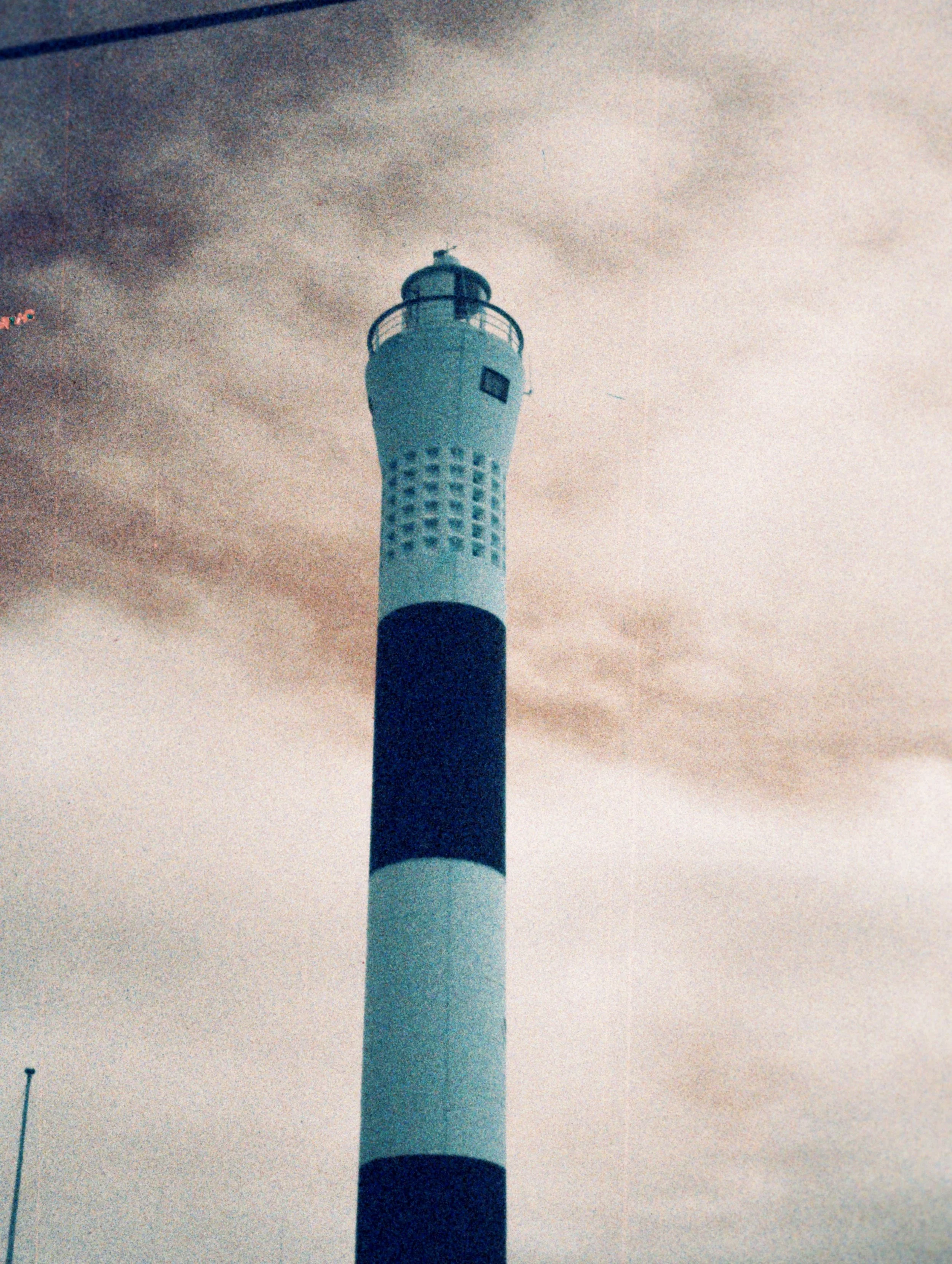 Nighttime view of a lighthouse with a circular top and lighthouse structure against a cloudy sky.