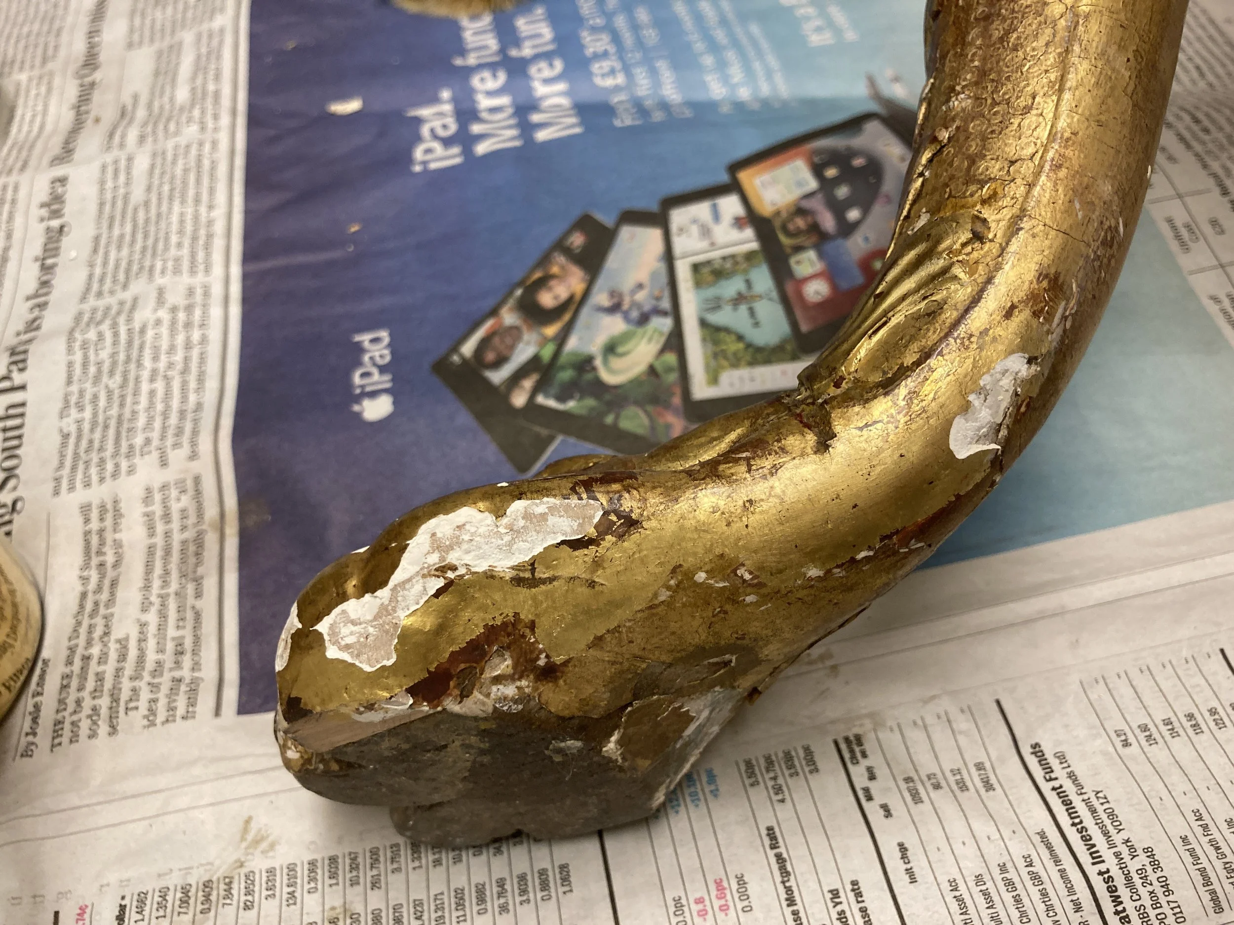A close-up view of a gold-painted shaped object on top of a newspaper, with a blurred blue background that appears to be a box packaging for an iPad.