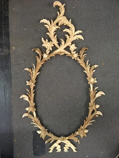 Ornate gold-colored oval picture frame with intricate floral and leaf designs, lying on a dark surface.