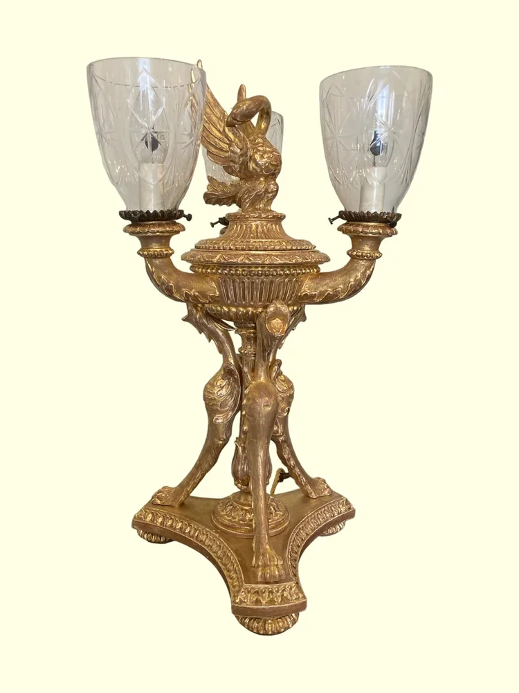 A vintage gold-colored candelabra with a central swan figure, featuring two glass candle holders on either side.