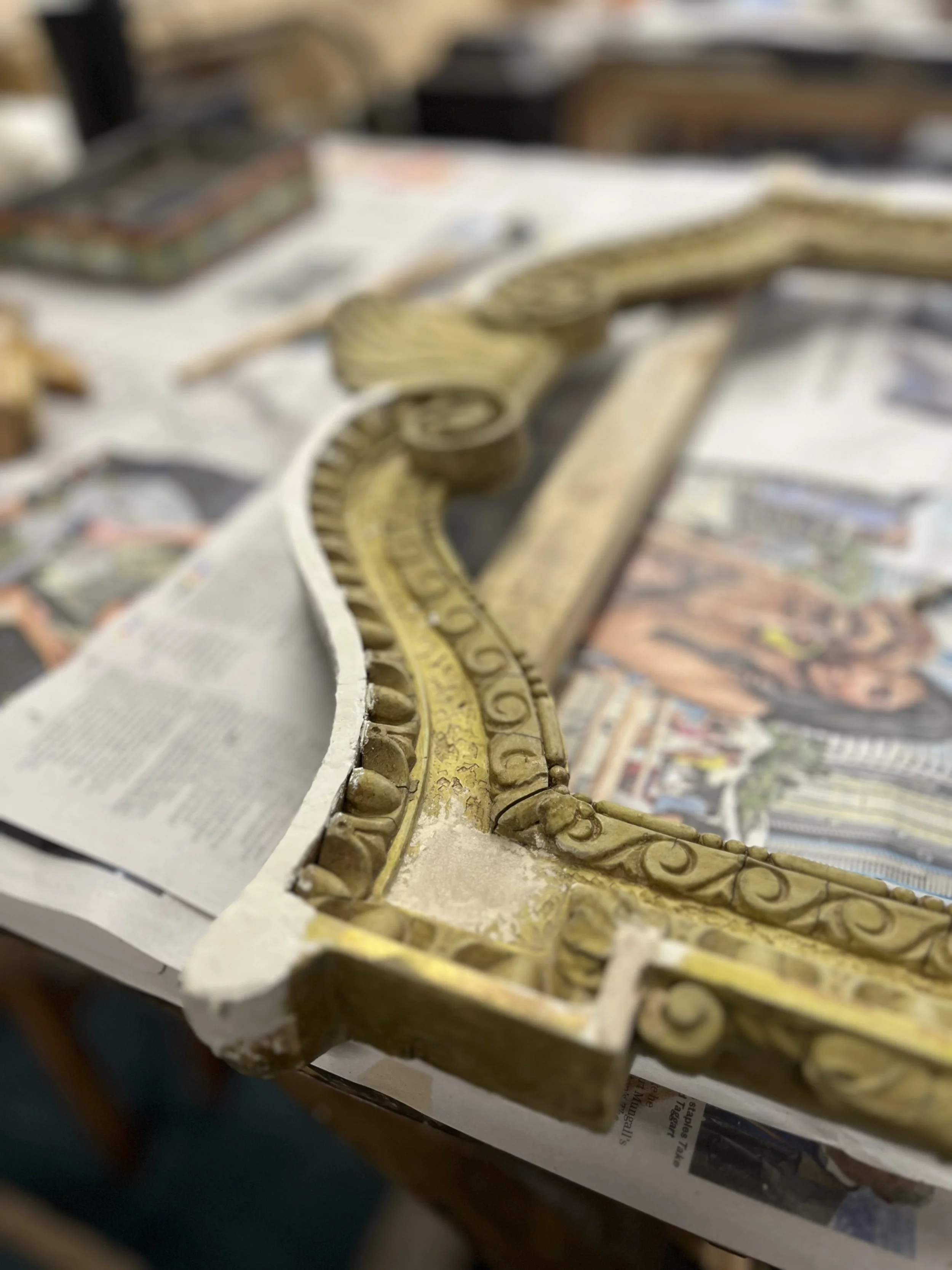 Close-up of a decorative golden gold leaf molding with intricate scrollwork on a painted surface.