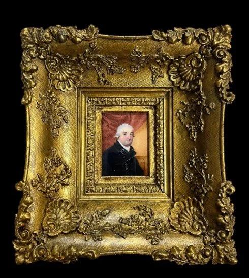 A small portrait of George Washington in an ornate, gold decorative frame with elaborate floral and scroll designs.
