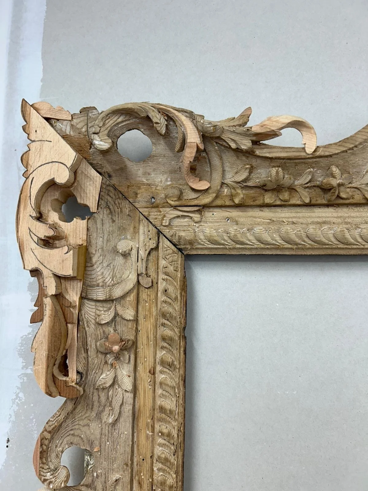 Close-up of ornately carved, unfinished wooden frame or furniture with intricate floral and scroll designs. The wood shows natural grain and carving details.