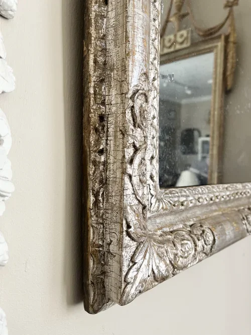 Close-up of an ornate, weathered wooden frame of a mirror with intricate carvings and peeling paint.