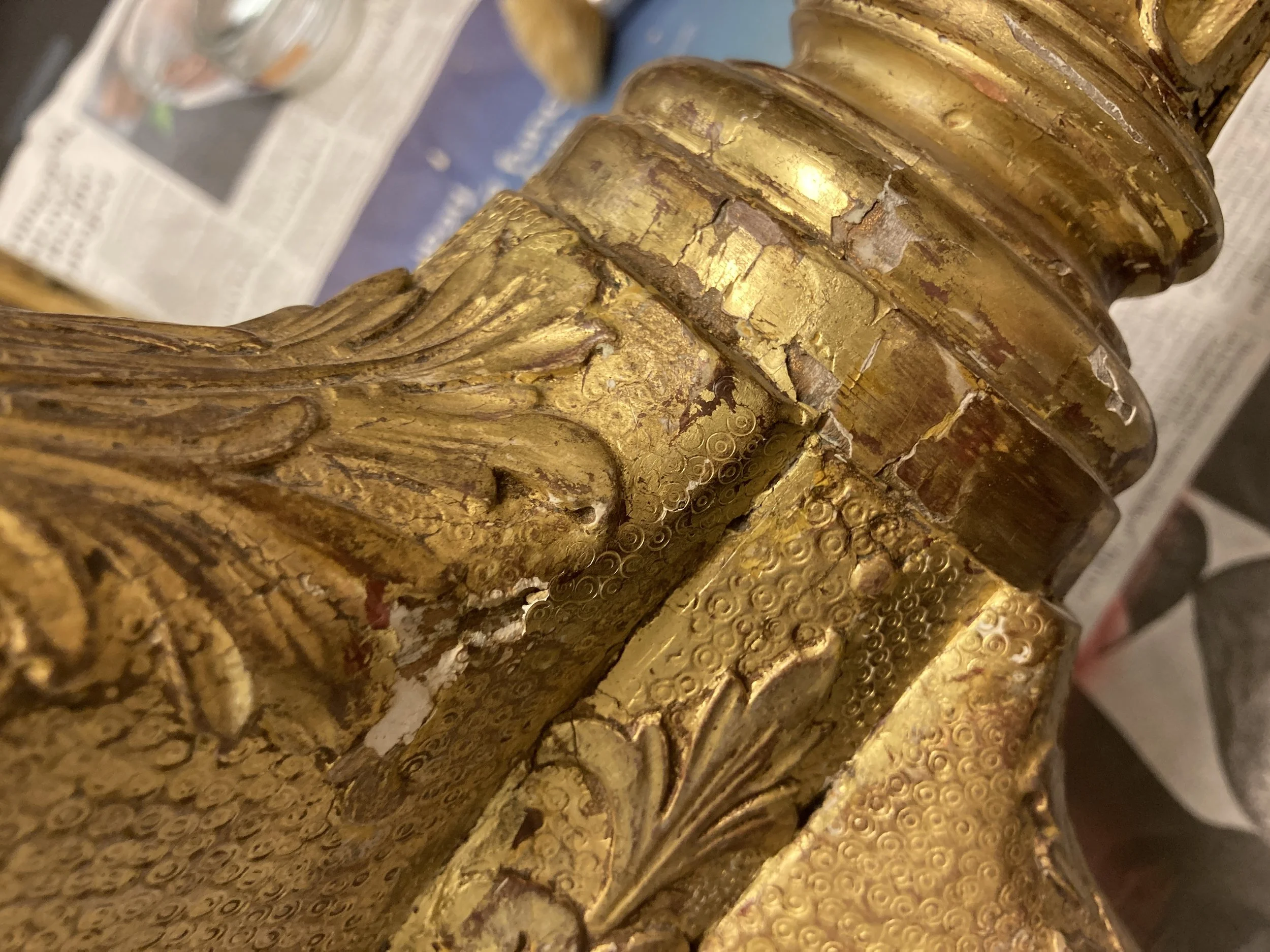 Close-up of a gold, carved decorative piece with intricate patterns and signs of wear and peeling.