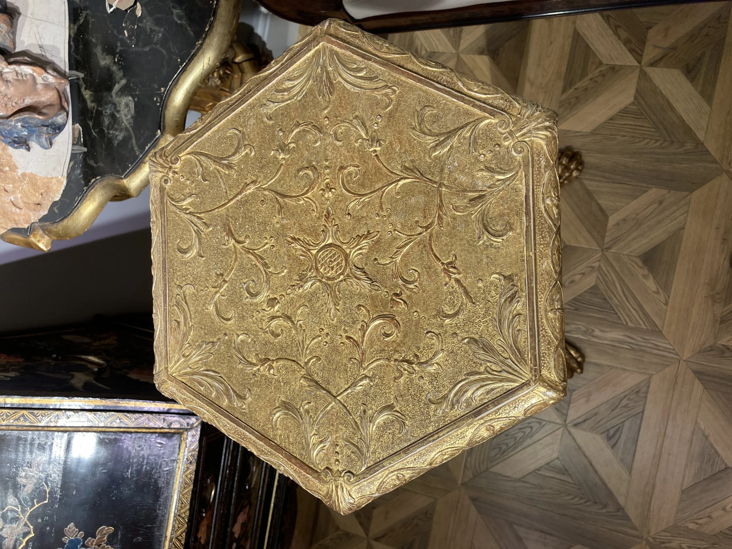 Close-up of an ornate gold-colored table with intricate floral patterns, set on a wooden floor with a geometric design.