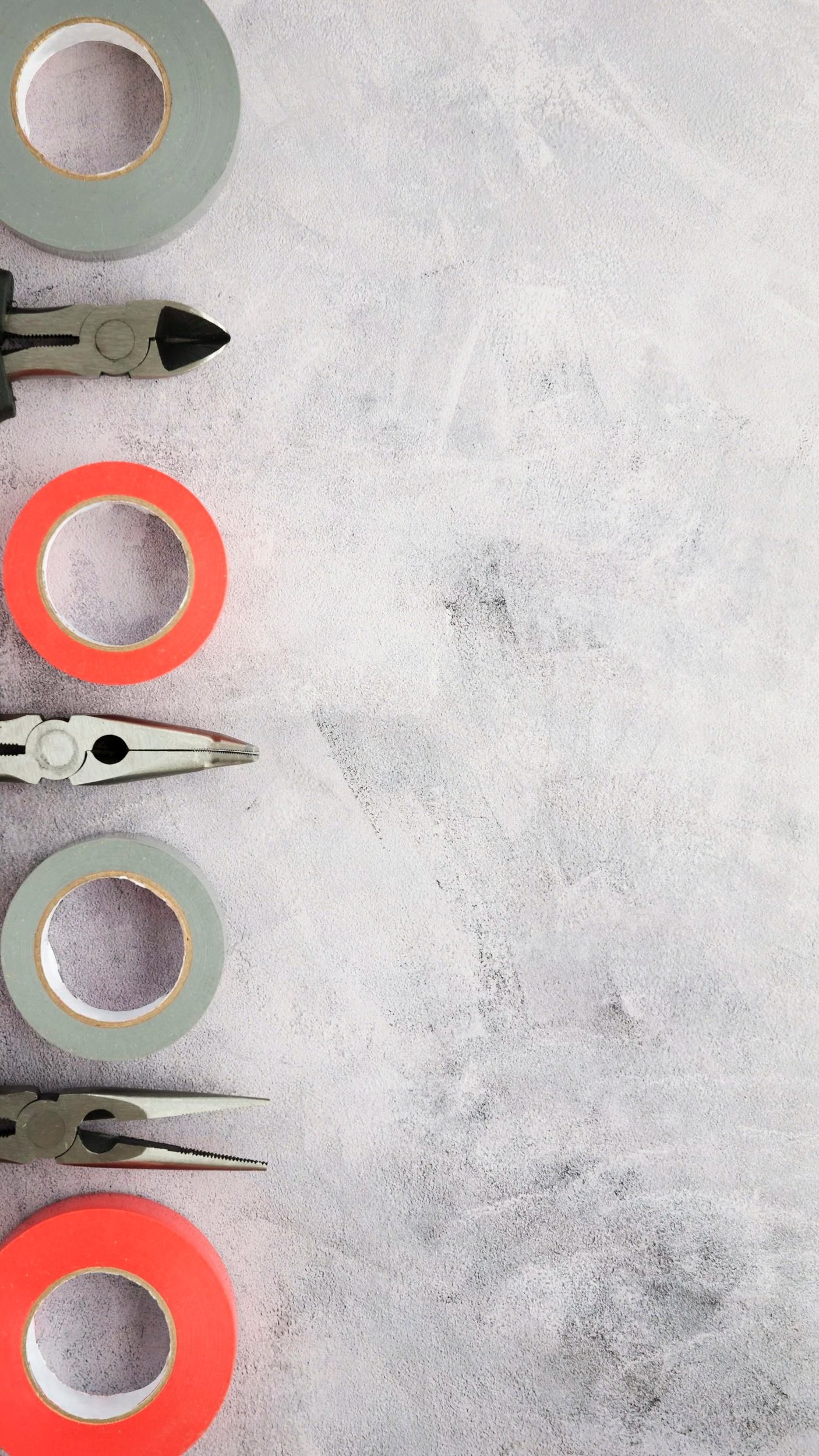 Flat lay of a measuring tape, a pair of pliers, and a roll of green tape on a textured gray surface.