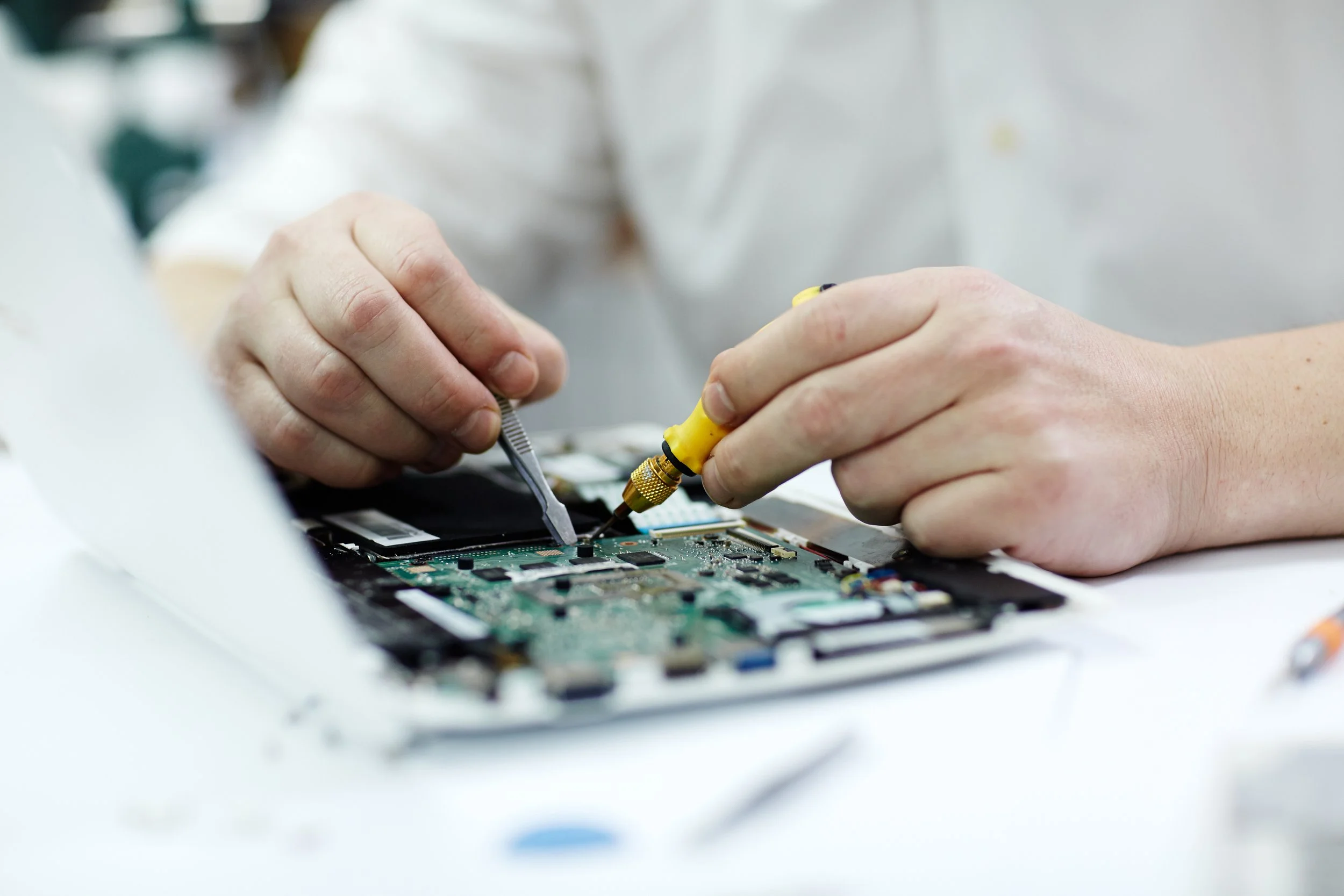 Person working on electronic device, using tools to repair circuit board.