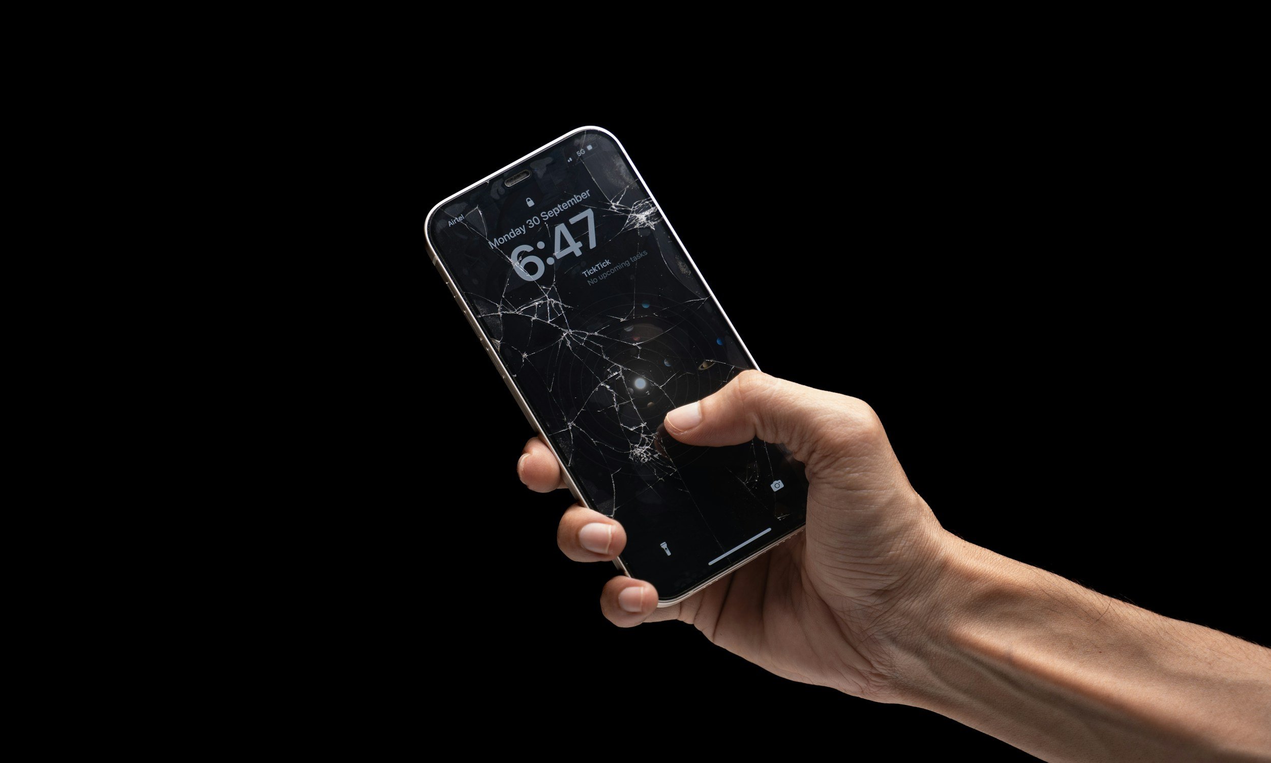 Hand holding a smartphone with a shattered screen against a black background.