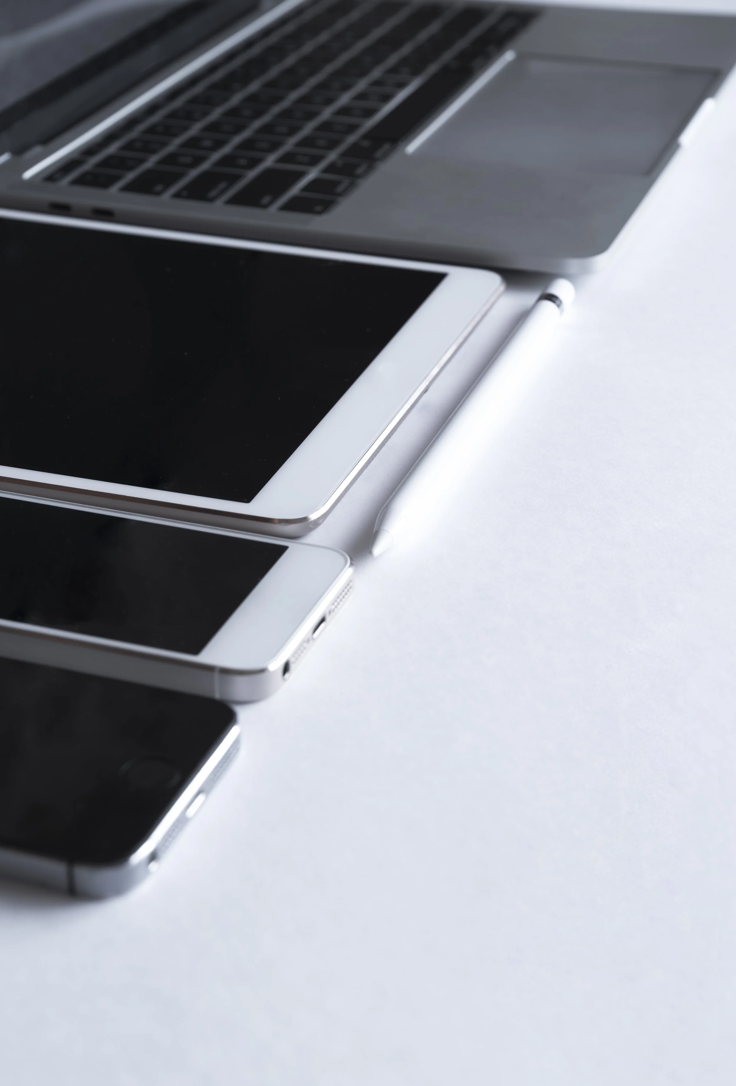 Multiple electronic devices, including a tablet, smartphones, and a laptop, arranged on a white surface.