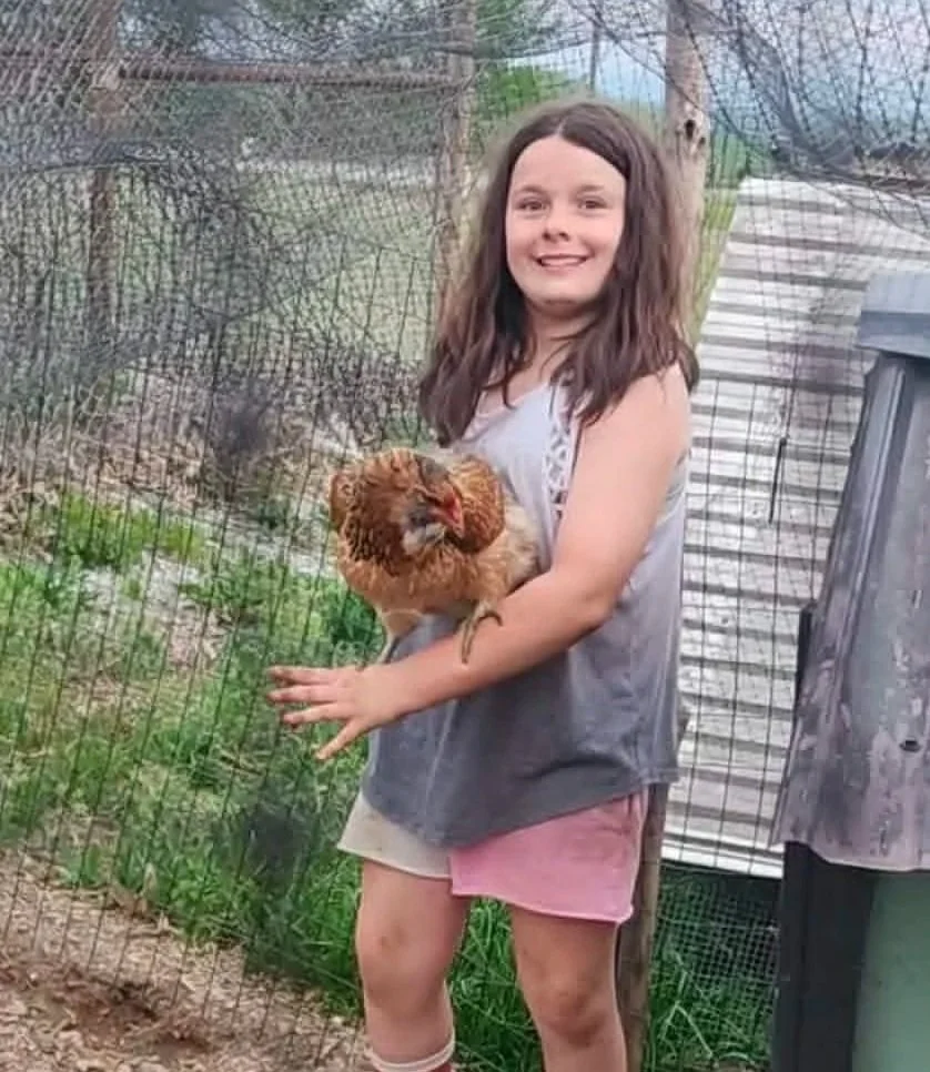 Child holding a chicken beside the Heathen Farms family garden