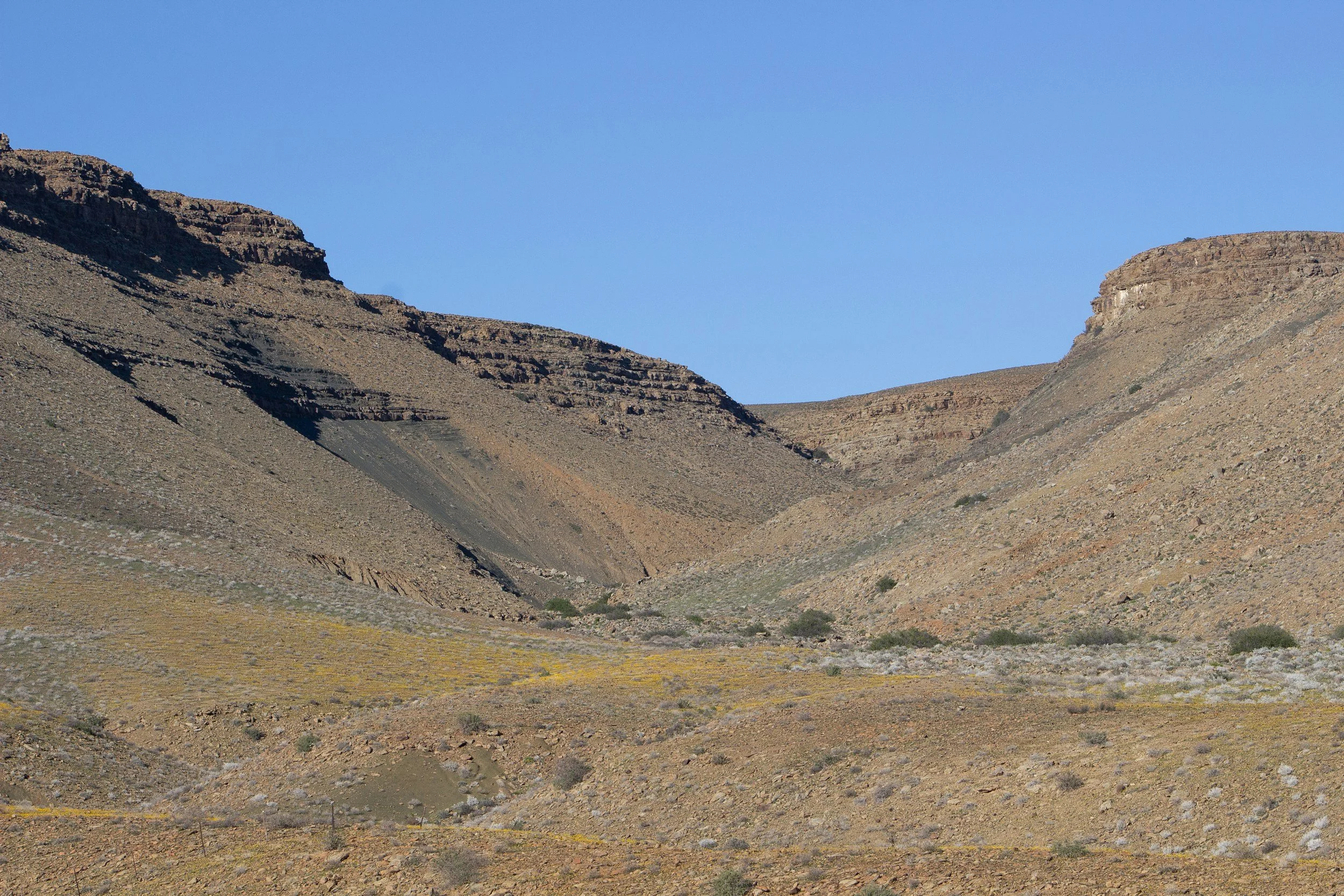 A barren mountainous landscape with rocky slopes and a clear blue sky.