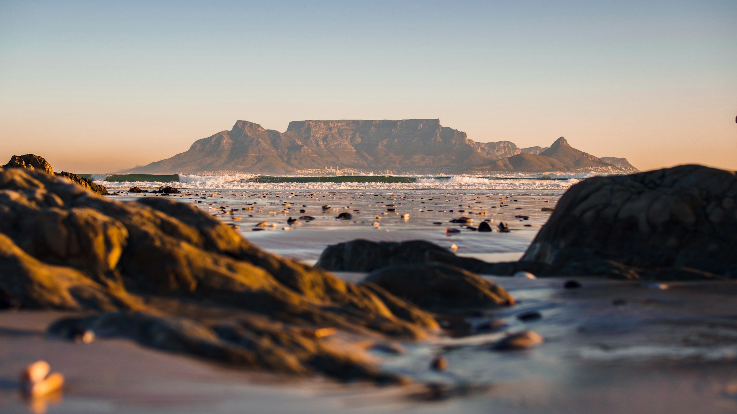 Sunset over a sandy beach (Blouberg Stran)  with scattered rocks, with Table Mountain in the background.