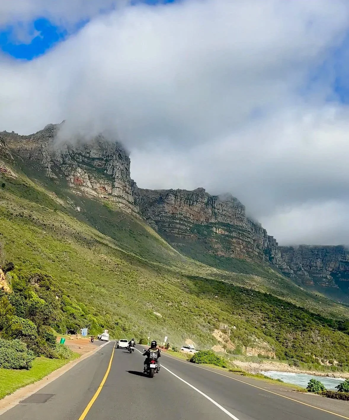 A mountain landscape with a road and vehicles, partly covered by clouds.