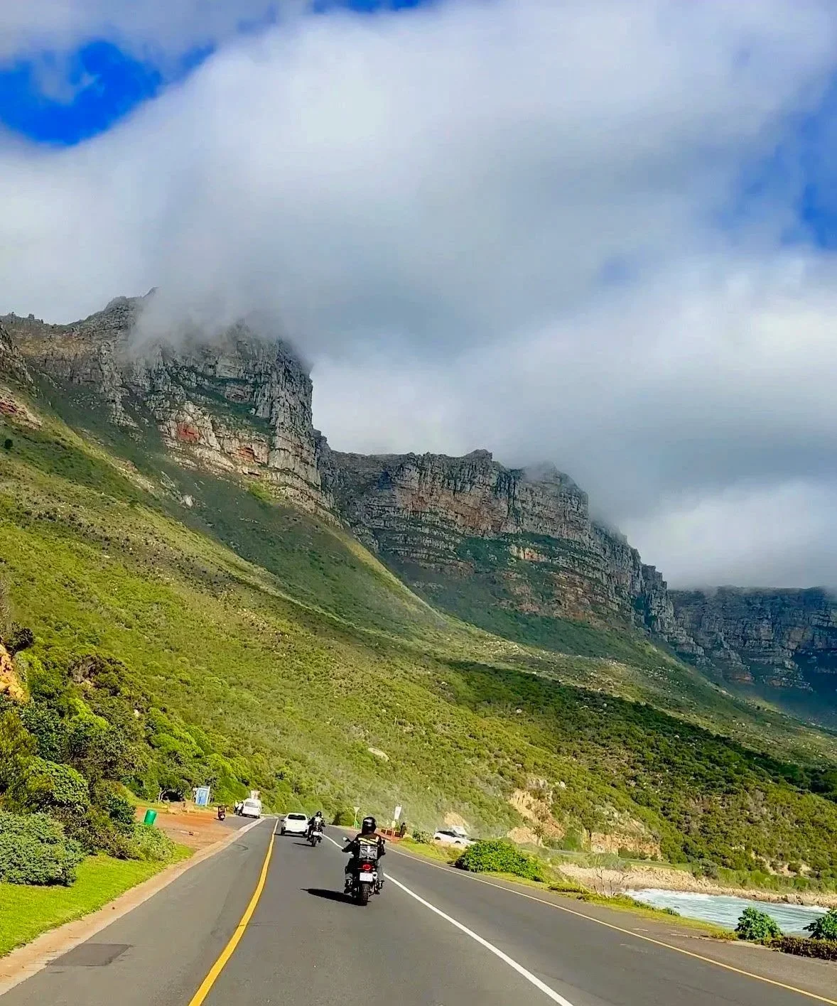 A mountain landscape with a road and vehicles, partly covered by clouds.