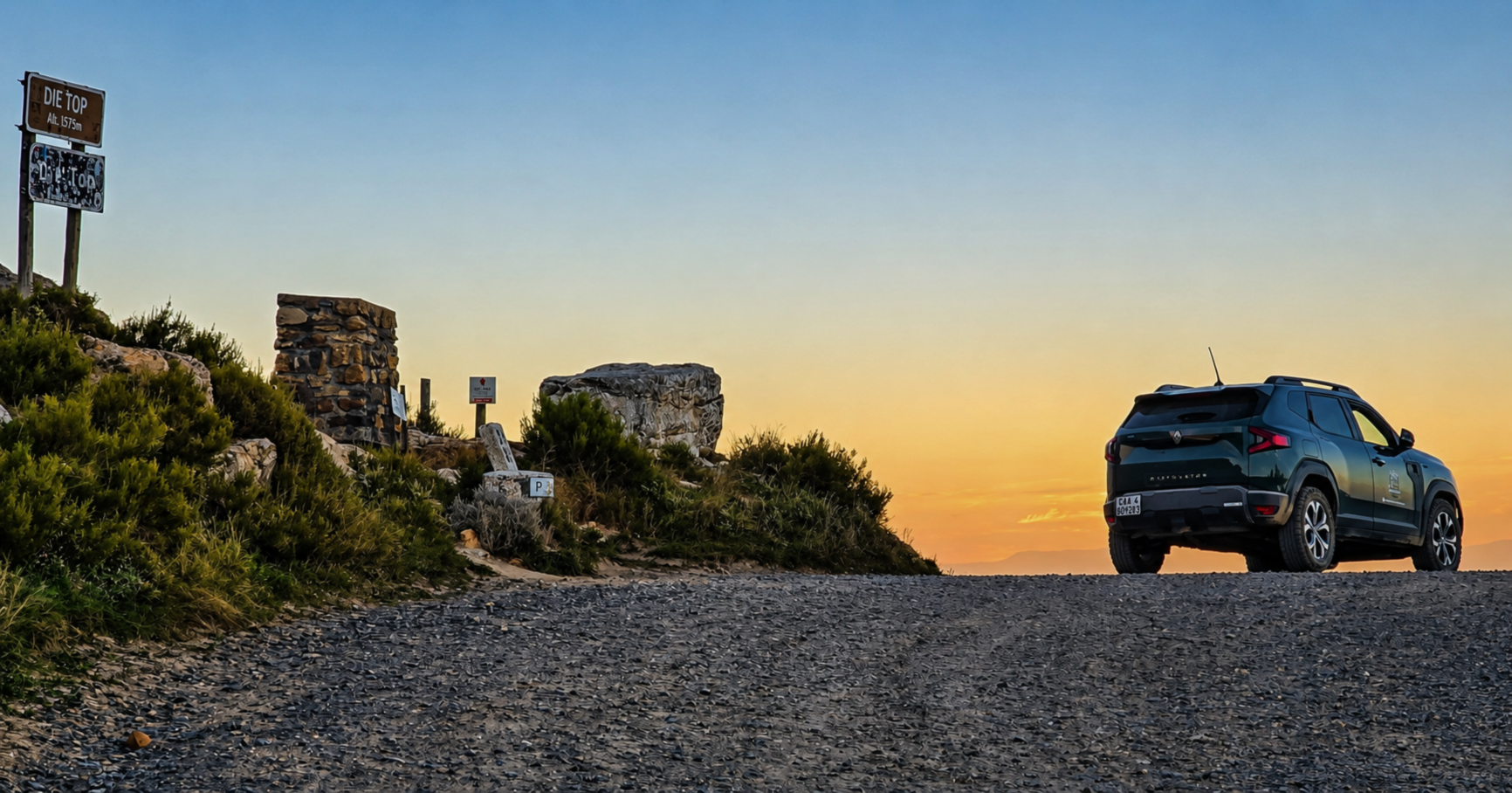 A black SUV parked on a gravel area near a grassy hill and rocks, with a sunset sky in the background.