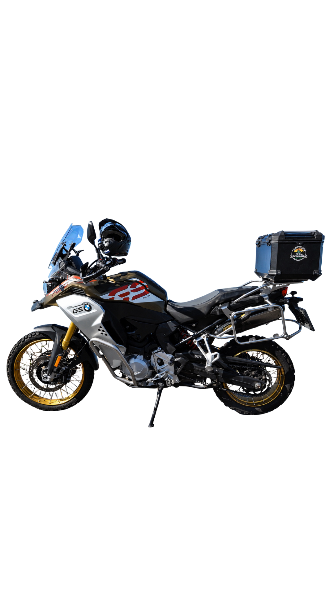 A BMW GS Adventure motorcycle in black, white, and gold, equipped with a front windshield, a black top case with a logo, and a helmet resting on the handlebars.