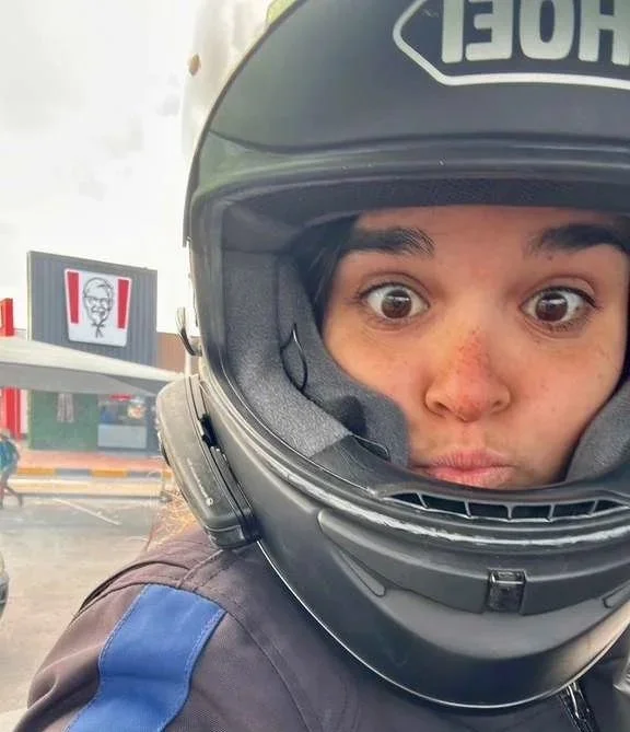 Person wearing a motorcycle helmet with a surprised expression, eyes wide open, in an outdoor setting with a KFC sign in the background. Muizenberg Cape Town South Africa