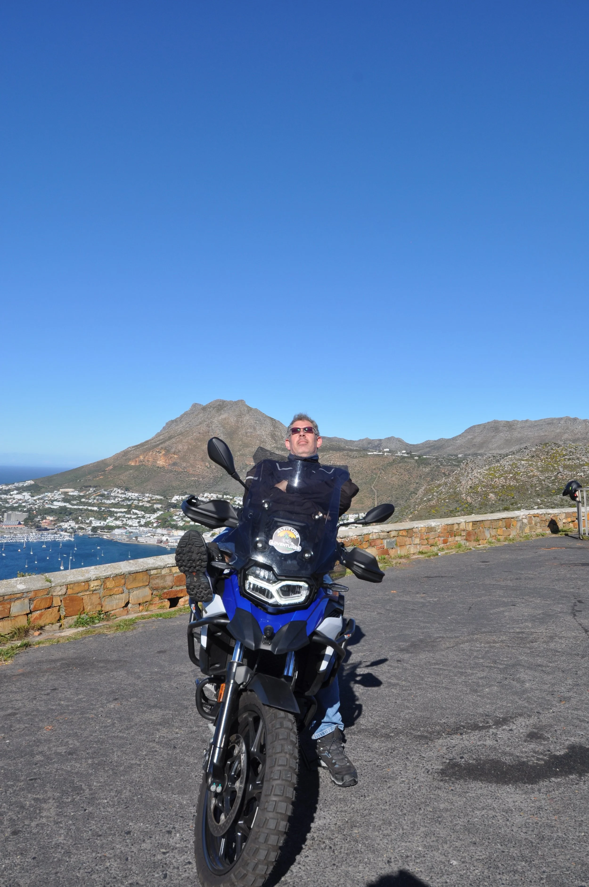 A man laying down on blue bow f800 motorcycle with mountains in the background under a clear blue sky of Redhill Simon's Town Cape Town Western Cape South Africa