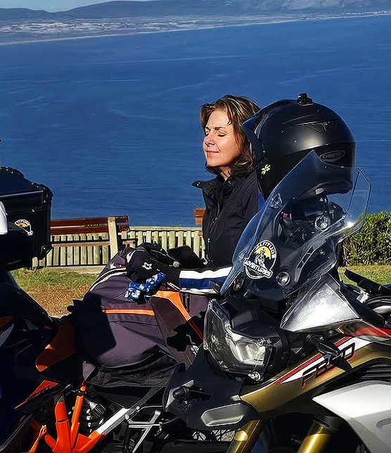 Woman with closed eyes and a smile standing beside a motorcycle overlooking a body of water. Cape Town Southern Suburbs South Africa