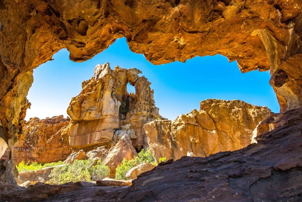 View of a desert landscape with large rock formations seen through a natural rock window, blue sky in the background.