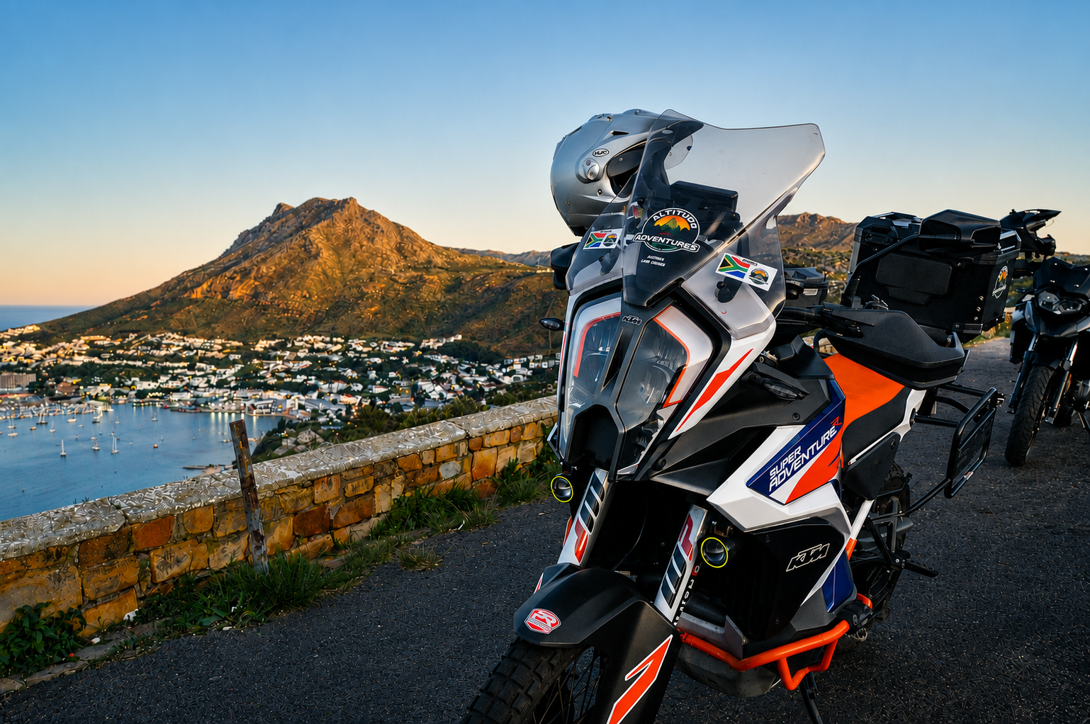 Motorcycles parked on scenic overlook of red hill Simon's Town, Souther Suburbs WC South Africa with a coastal town and mountain in the background at sunset. KTM 1290 Super Adventure R