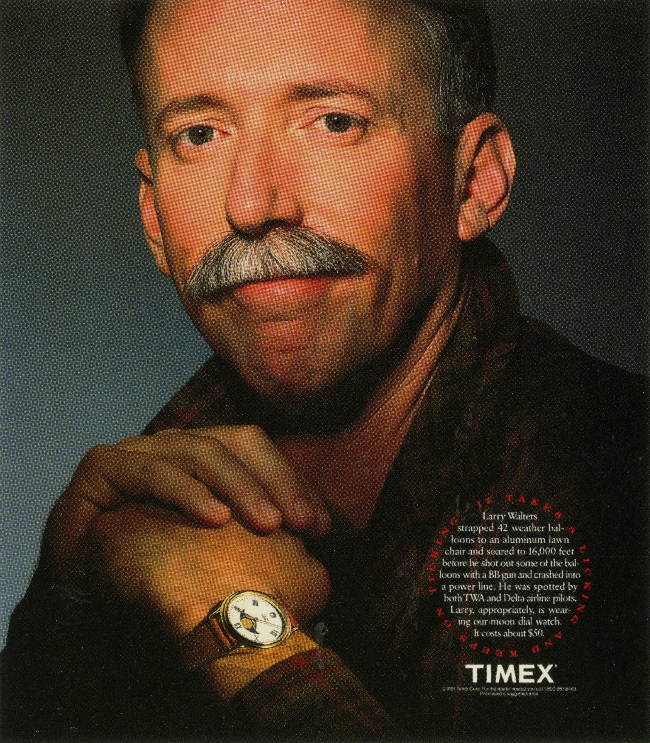 Close-up of a man's face and wrist. He is wearing a watch with a white face and Roman numerals, and has a mustache, dark hair, and is dressed in dark clothing. There is some red text around a circular area to the right of the image.