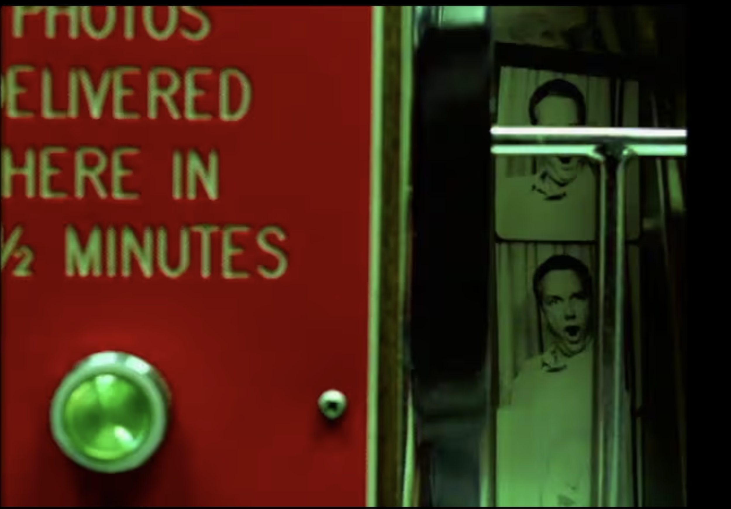 A red sign with partially visible white text reading 'autos delivered here in' and a green elevator button below it. Adjacent there is a row of vending machines or similar appliances with various designs and images, including a logo with a face.